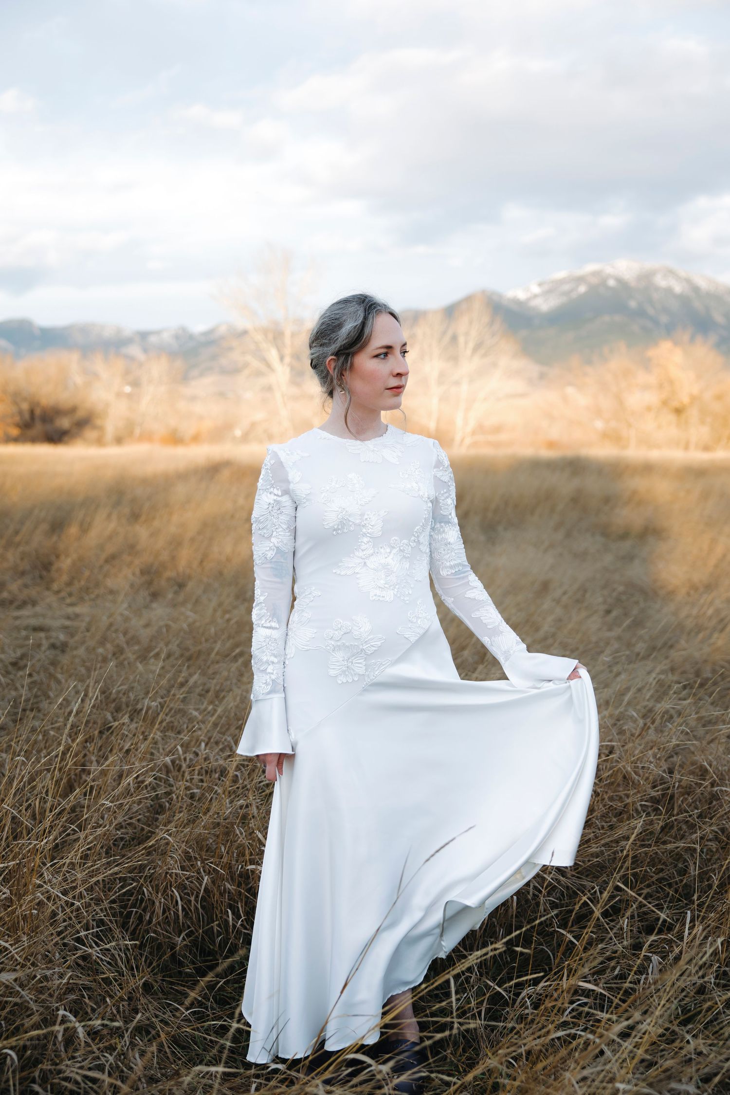 A bride in a vintage-style white dress poses gracefully in a golden autumn field.