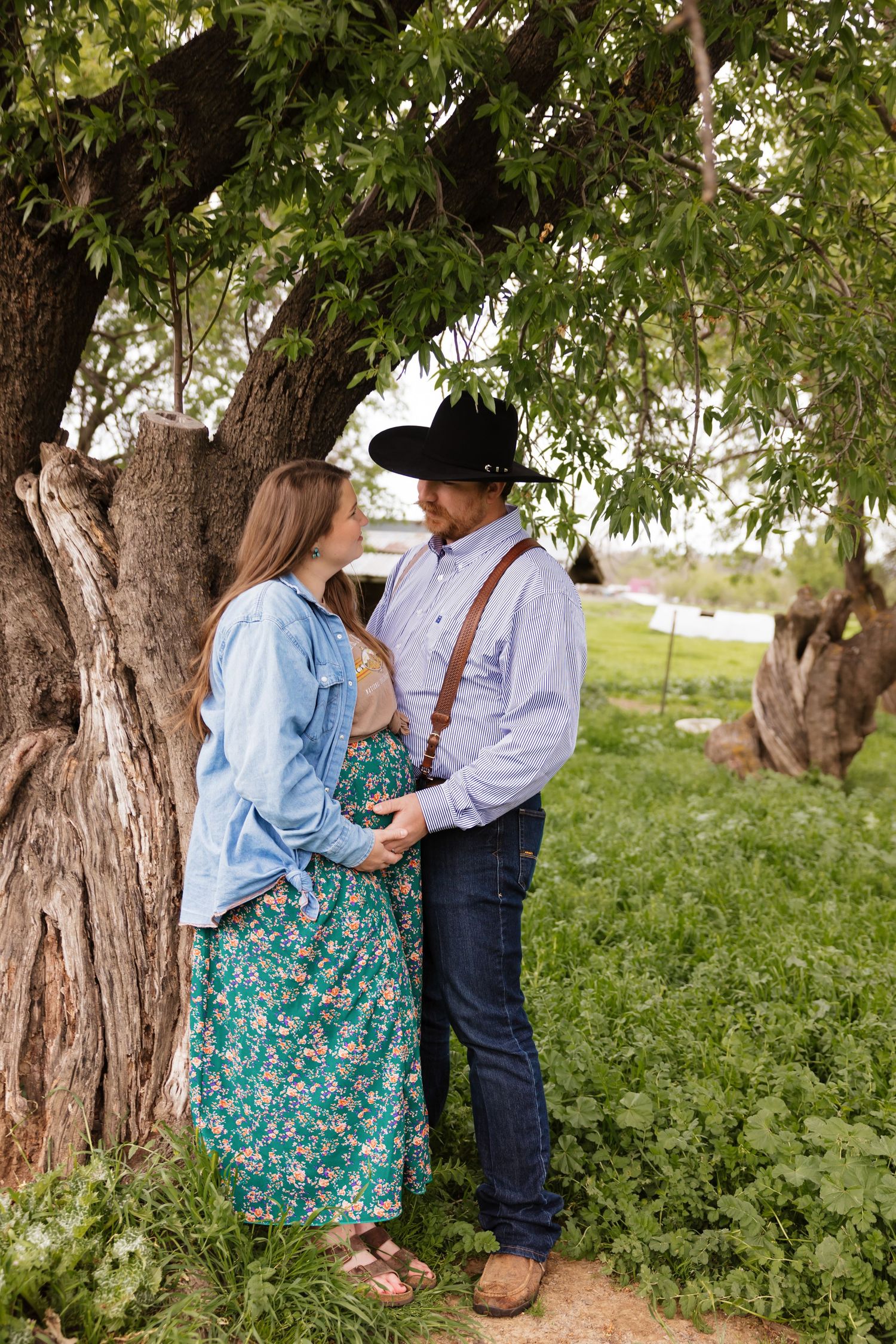 Intimate moment captured between couple under large tree branches in garden setting.