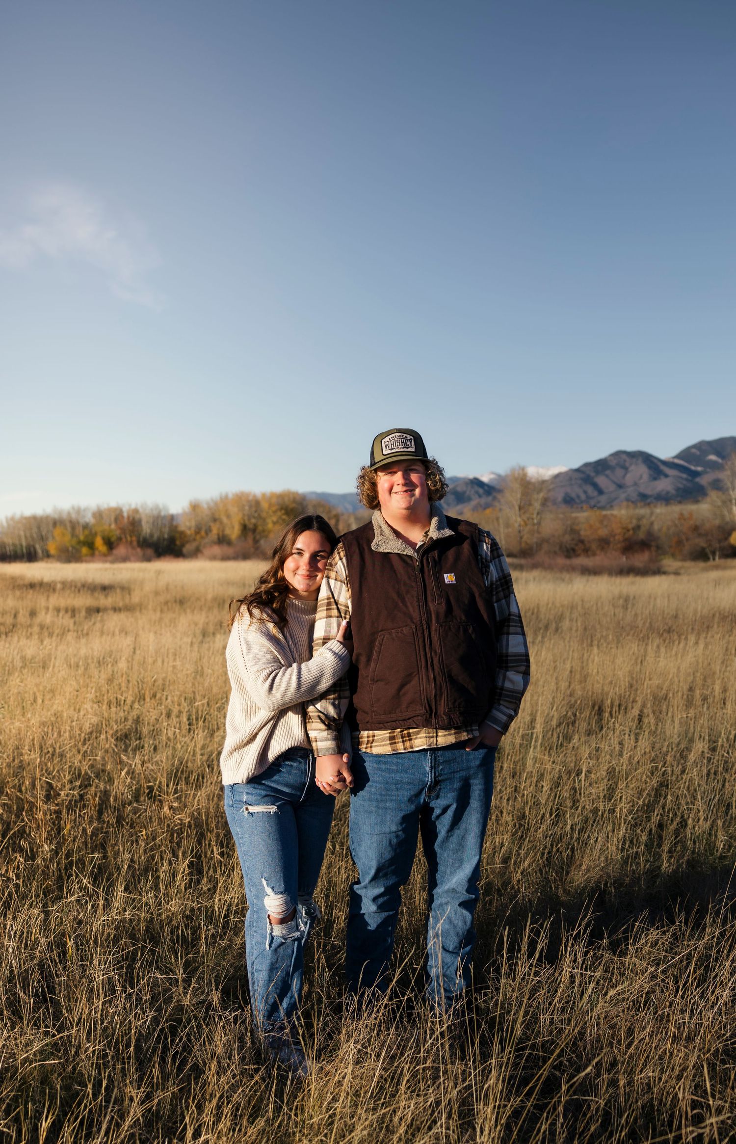 Couple in casual western attire standing together in a golden prairie field.