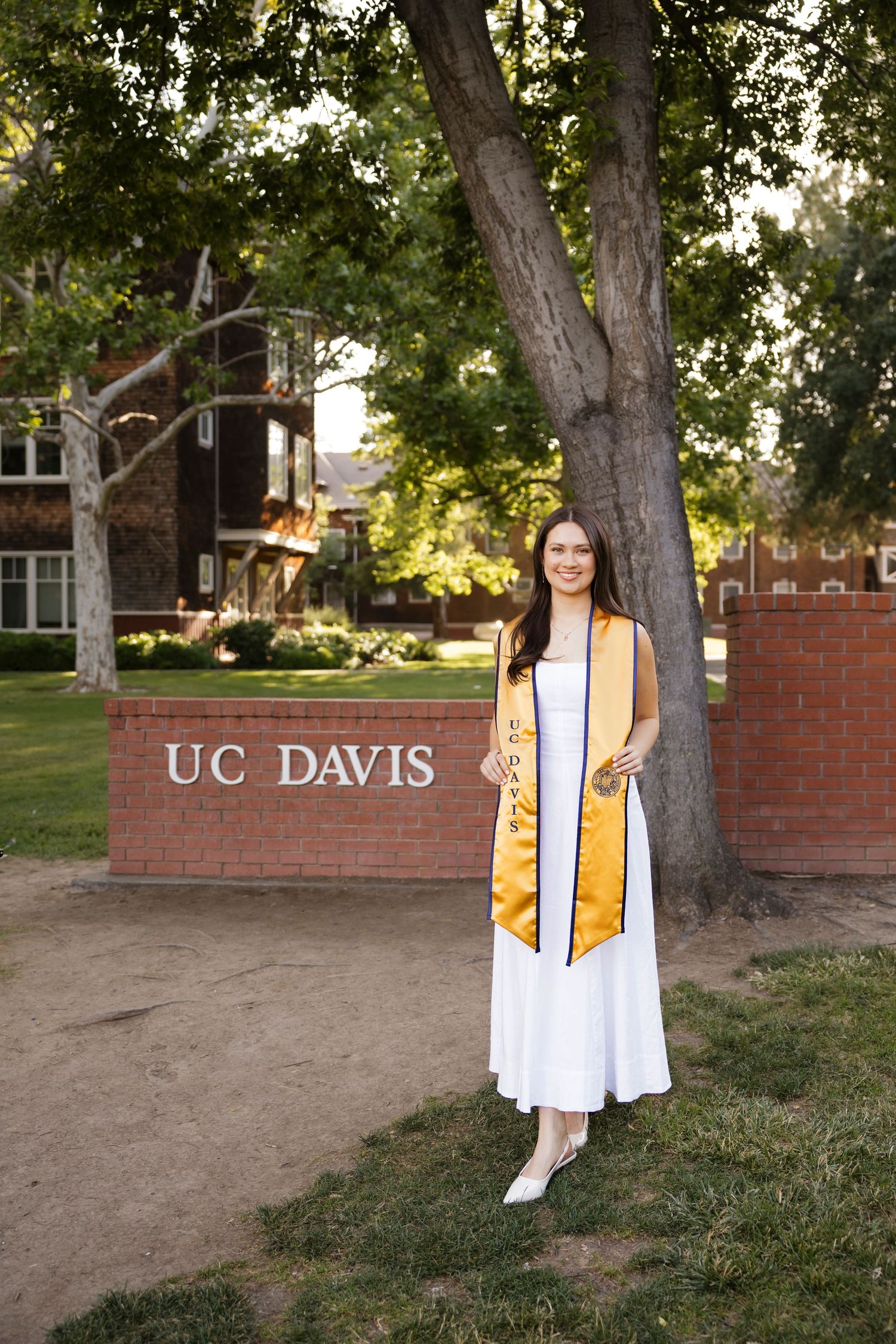 Graduate in gold stole poses near UC Davis campus sign.