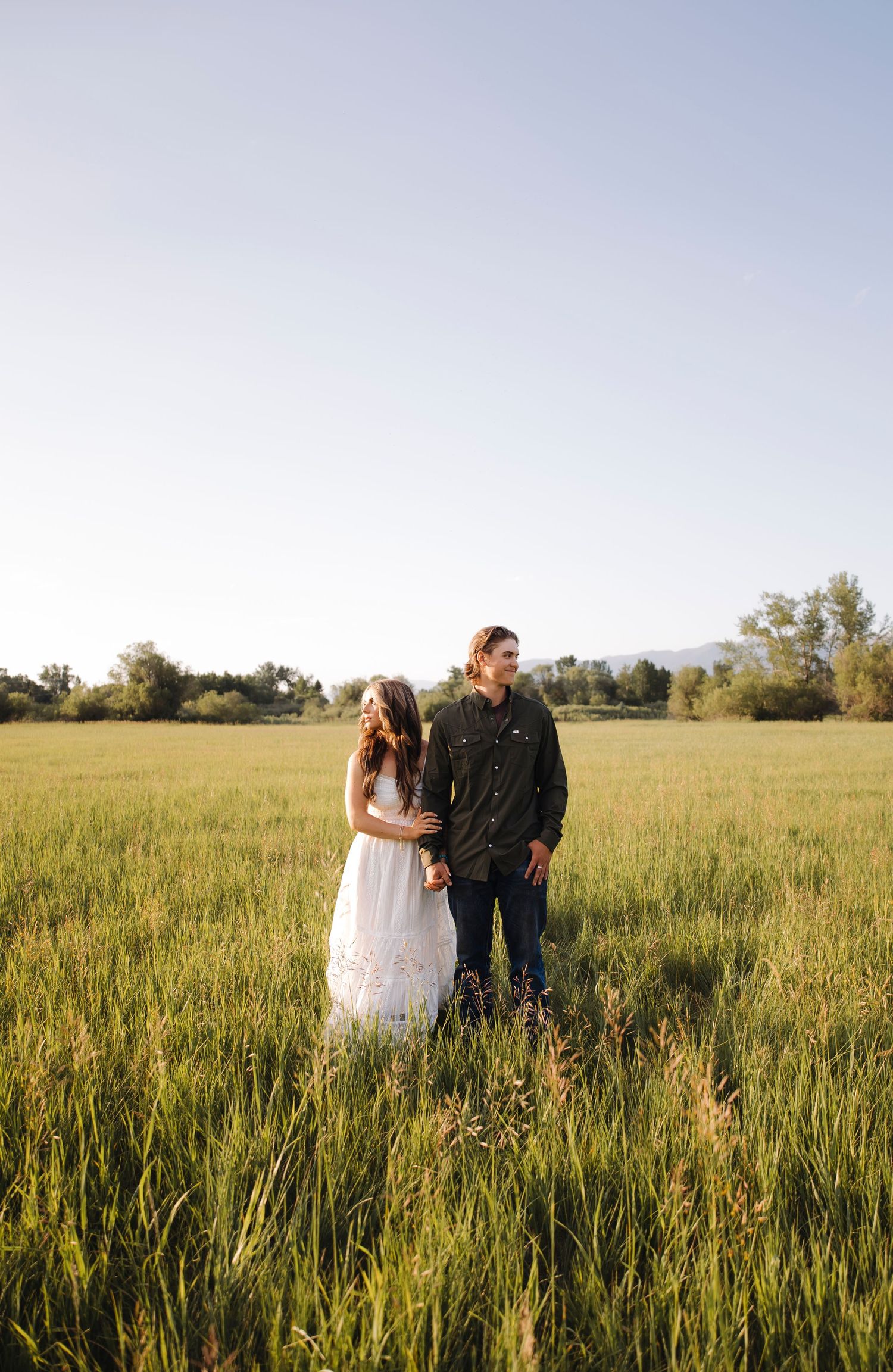Couple shares tender moment while standing in a sunlit field of tall grass.