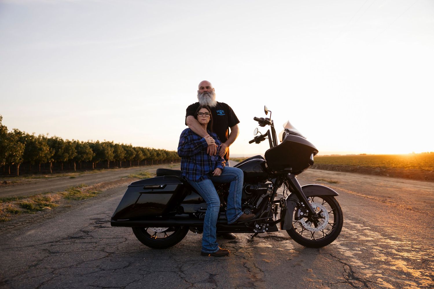 A couple sits on their parked motorcycle during sunset on a rural road.