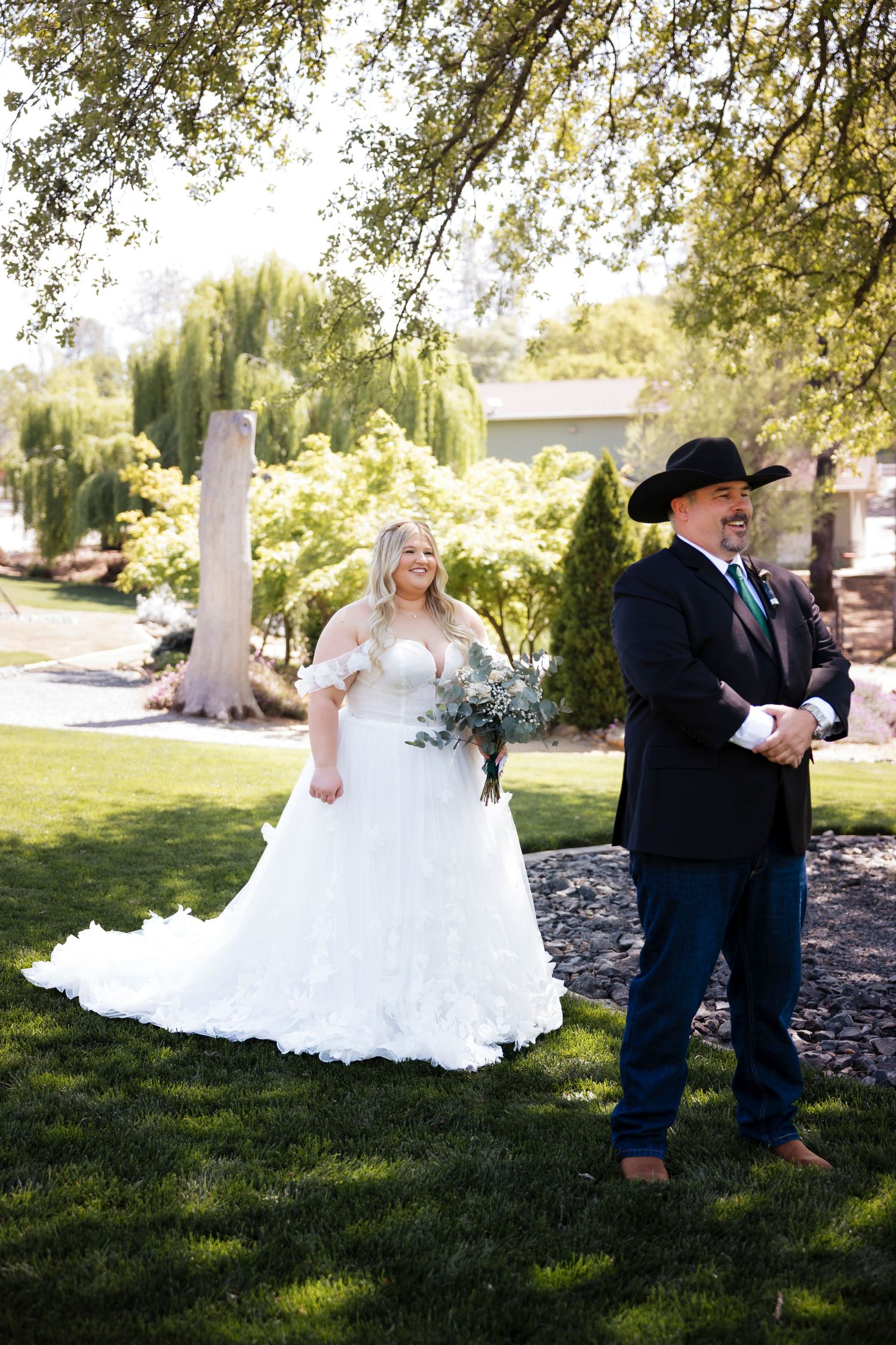 Wedding party poses on manicured lawn with trees in background during outdoor ceremony.