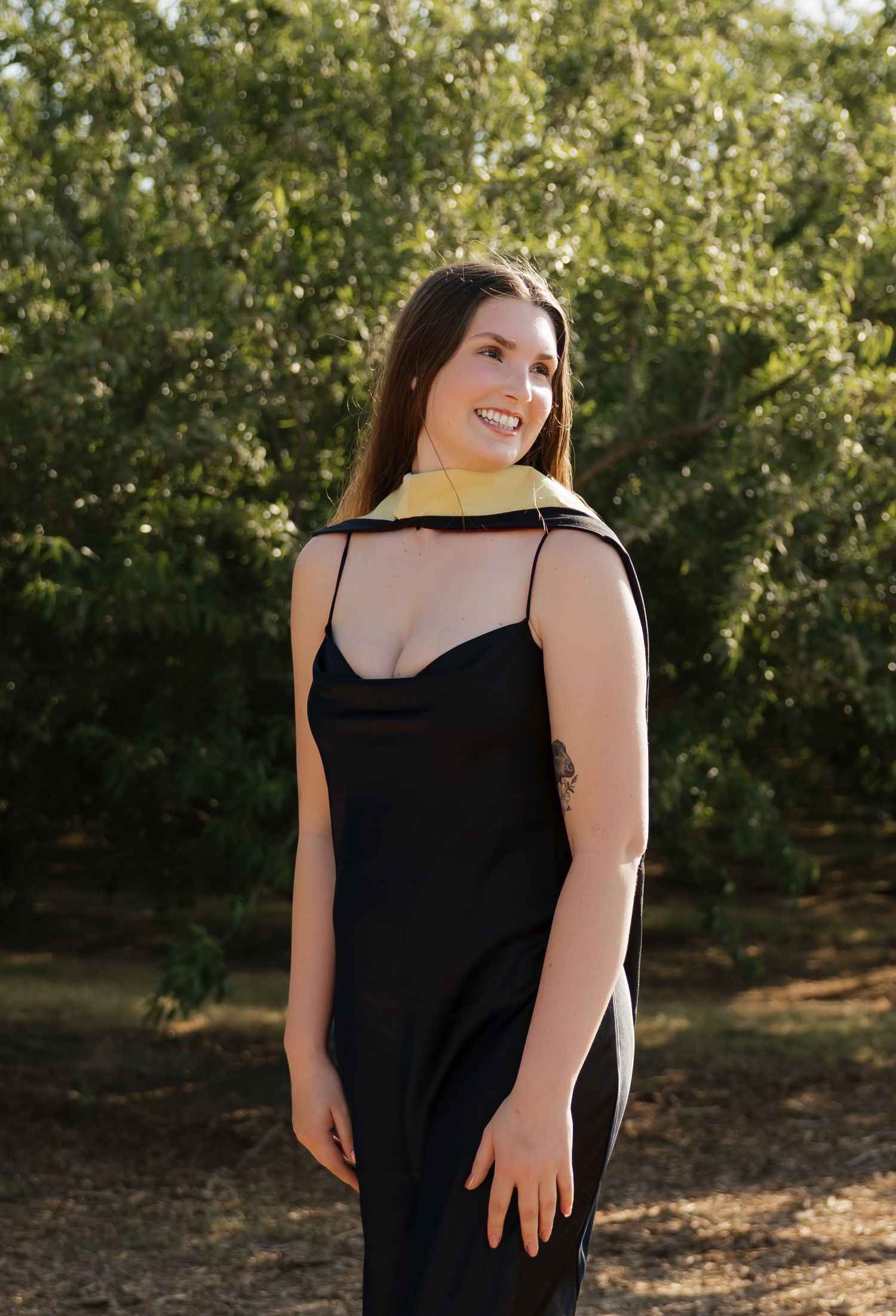Portrait of graduate in black dress against green foliage background.