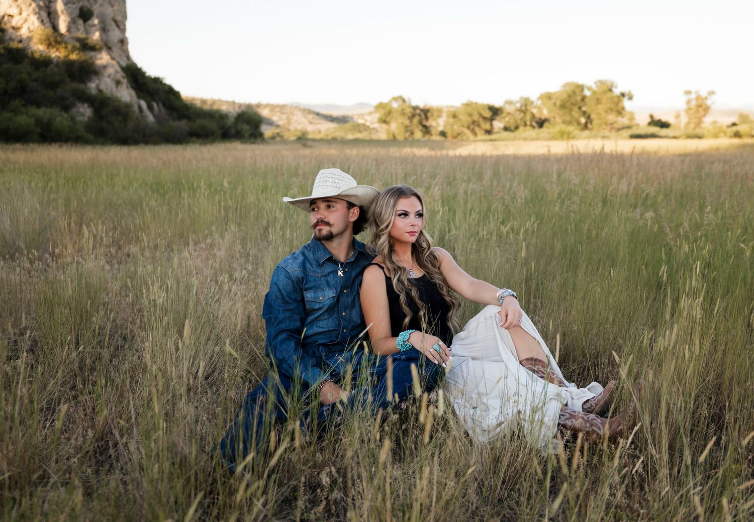 Couple sits together in a golden field during sunset.