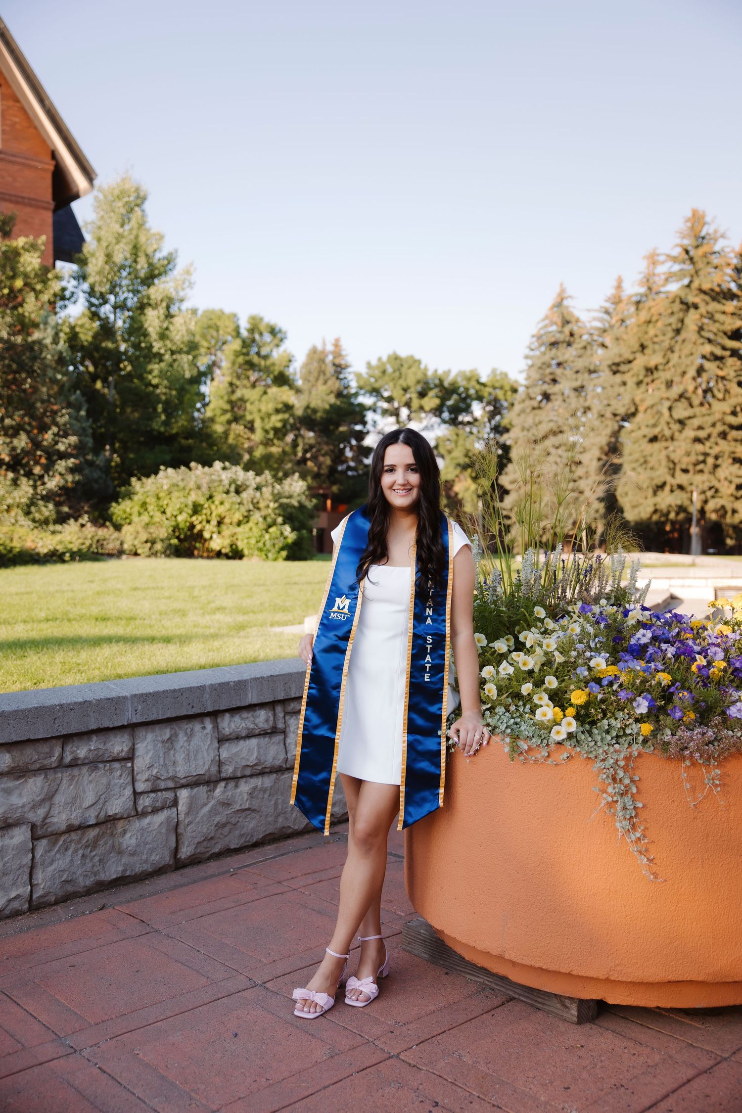 Graduate poses near decorative planters and stone wall on campus.