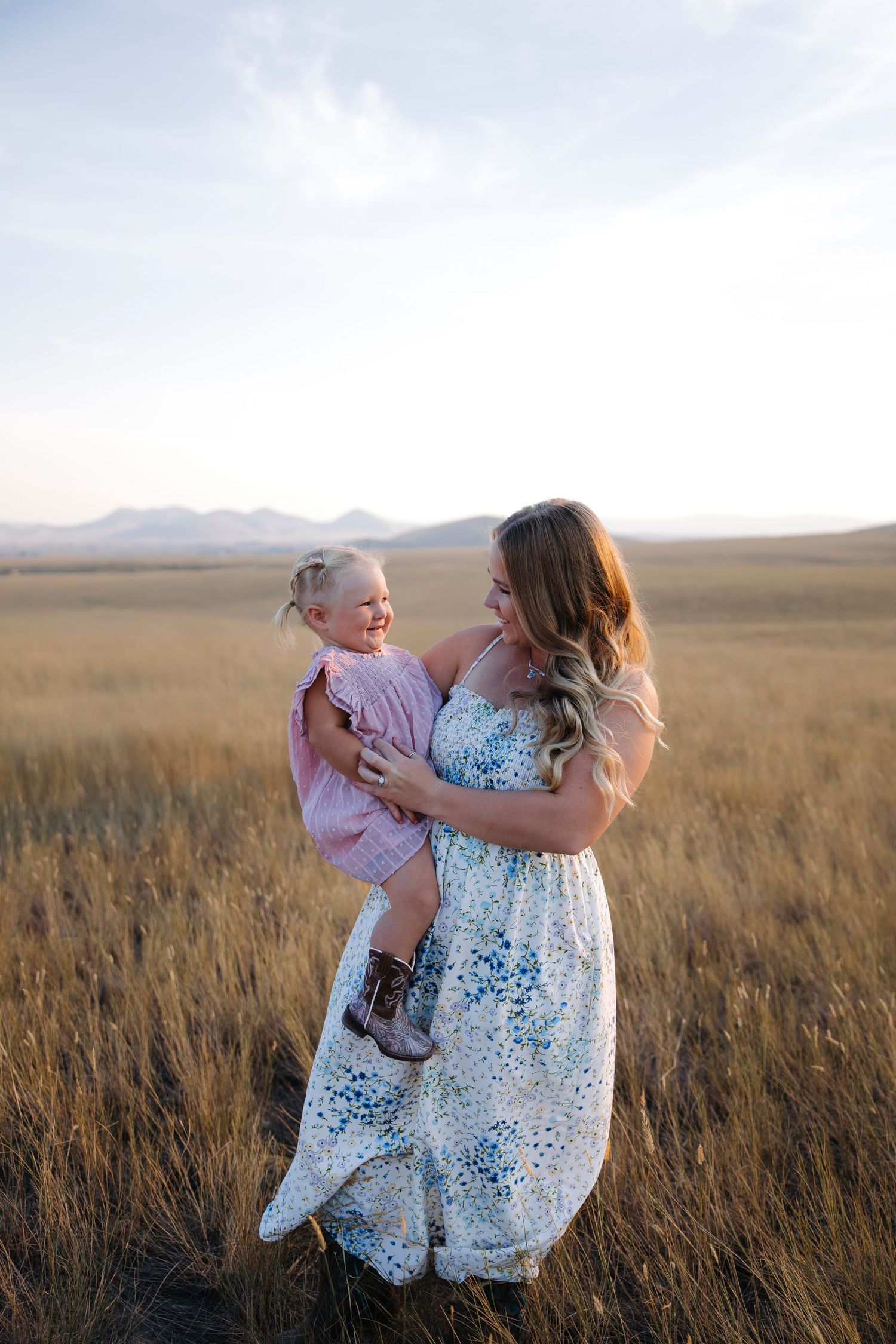 A tender family moment captured in a golden field at sunset with mountains in the background.