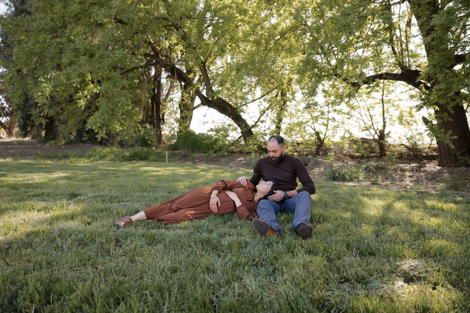 Peaceful scene of people relaxing on grass under leafy trees during golden hour.