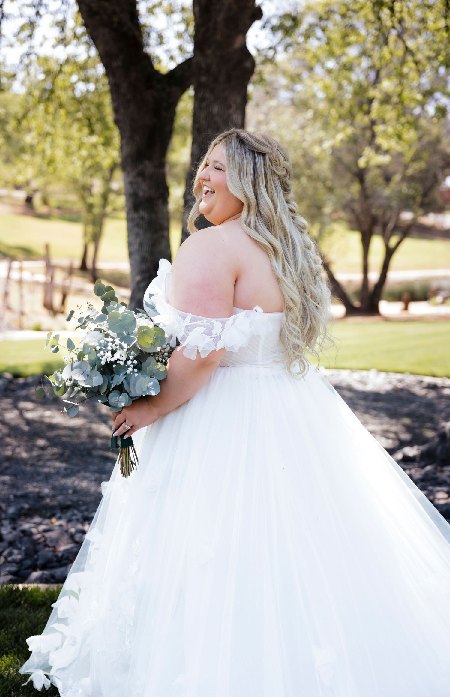 Flowing white ballgown wedding dress with off-shoulder details photographed in natural outdoor lighting.