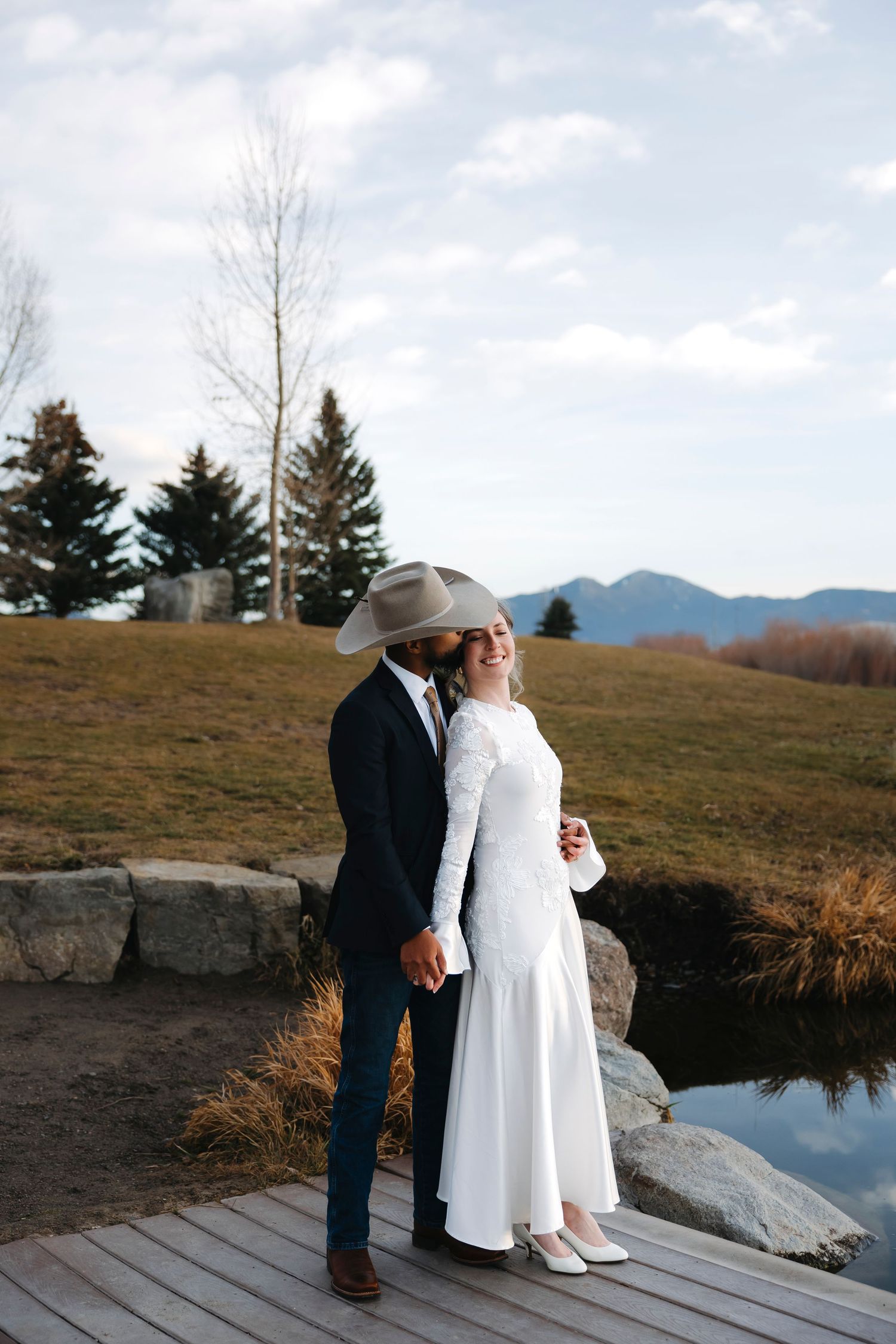 A wedding couple stands together on a wooden deck overlooking a mountain landscape.