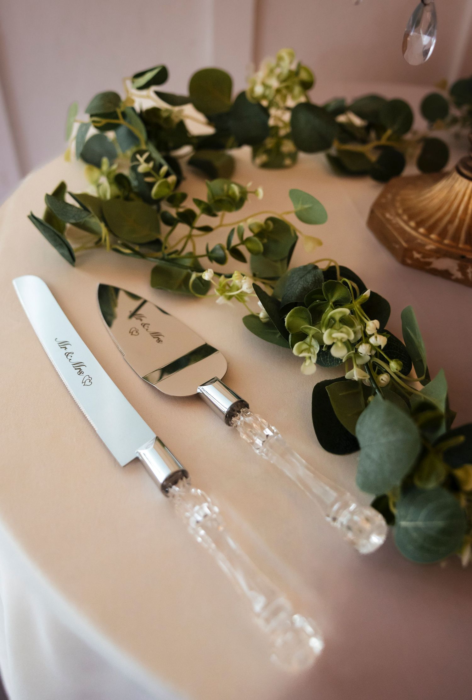 Wedding cake cutting set with crystal handles displayed with eucalyptus greenery.