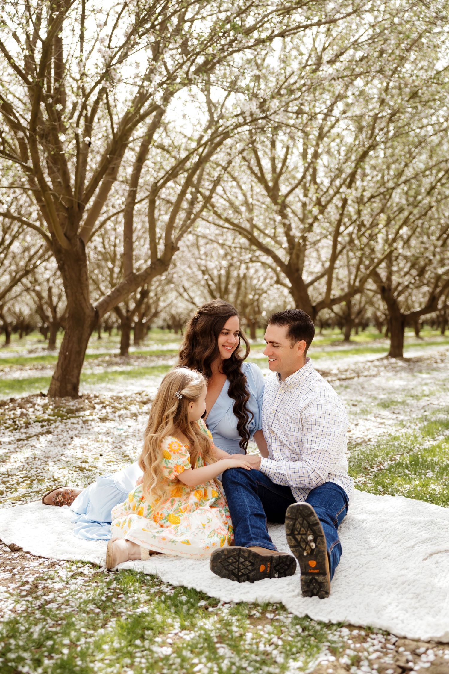 Spring photoshoot in blooming orchard with white petals covering the ground.