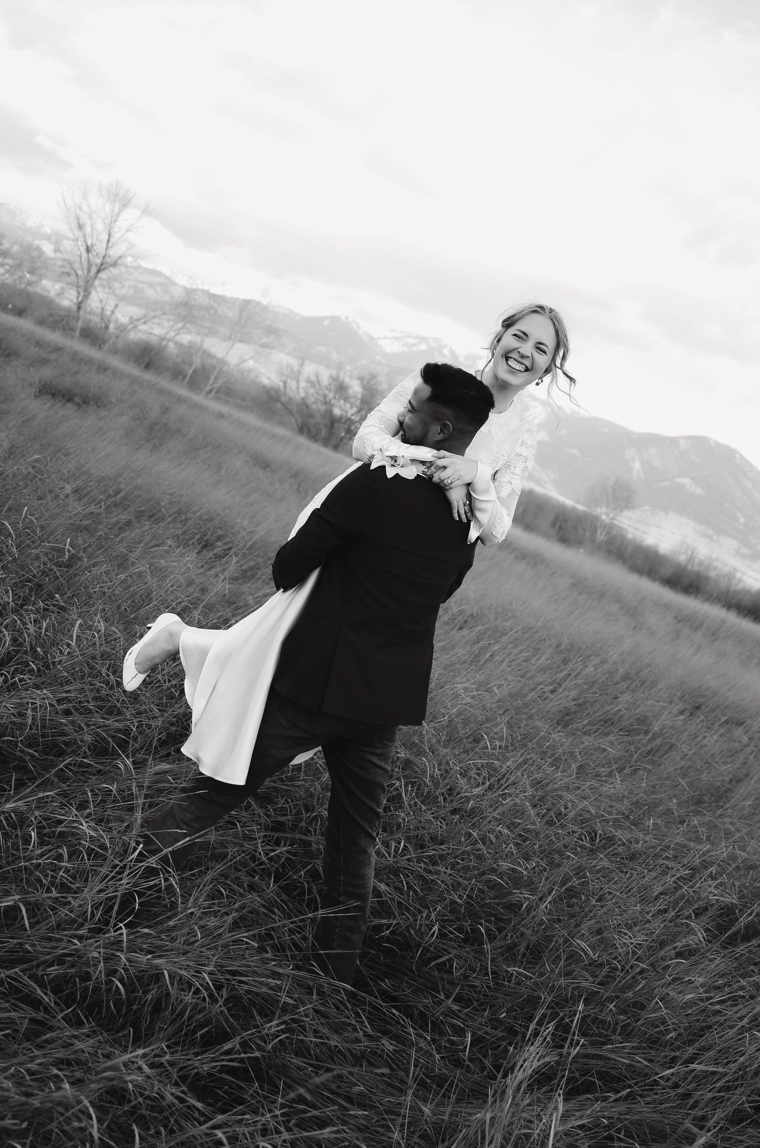 Black and white photo of playful moment during wedding photoshoot in field.