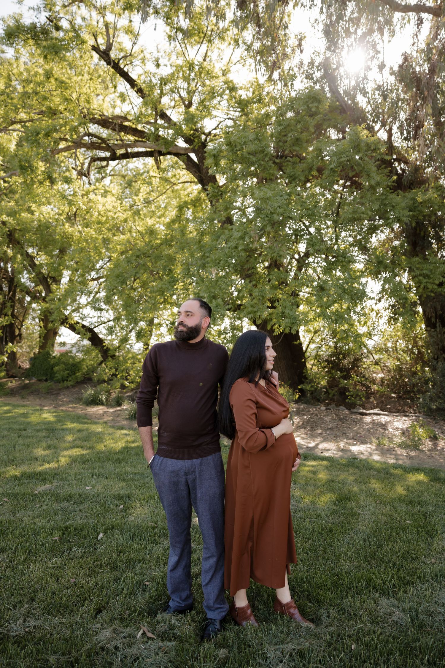Couple enjoying a romantic moment on grassy hillside surrounded by trees in natural outdoor setting.