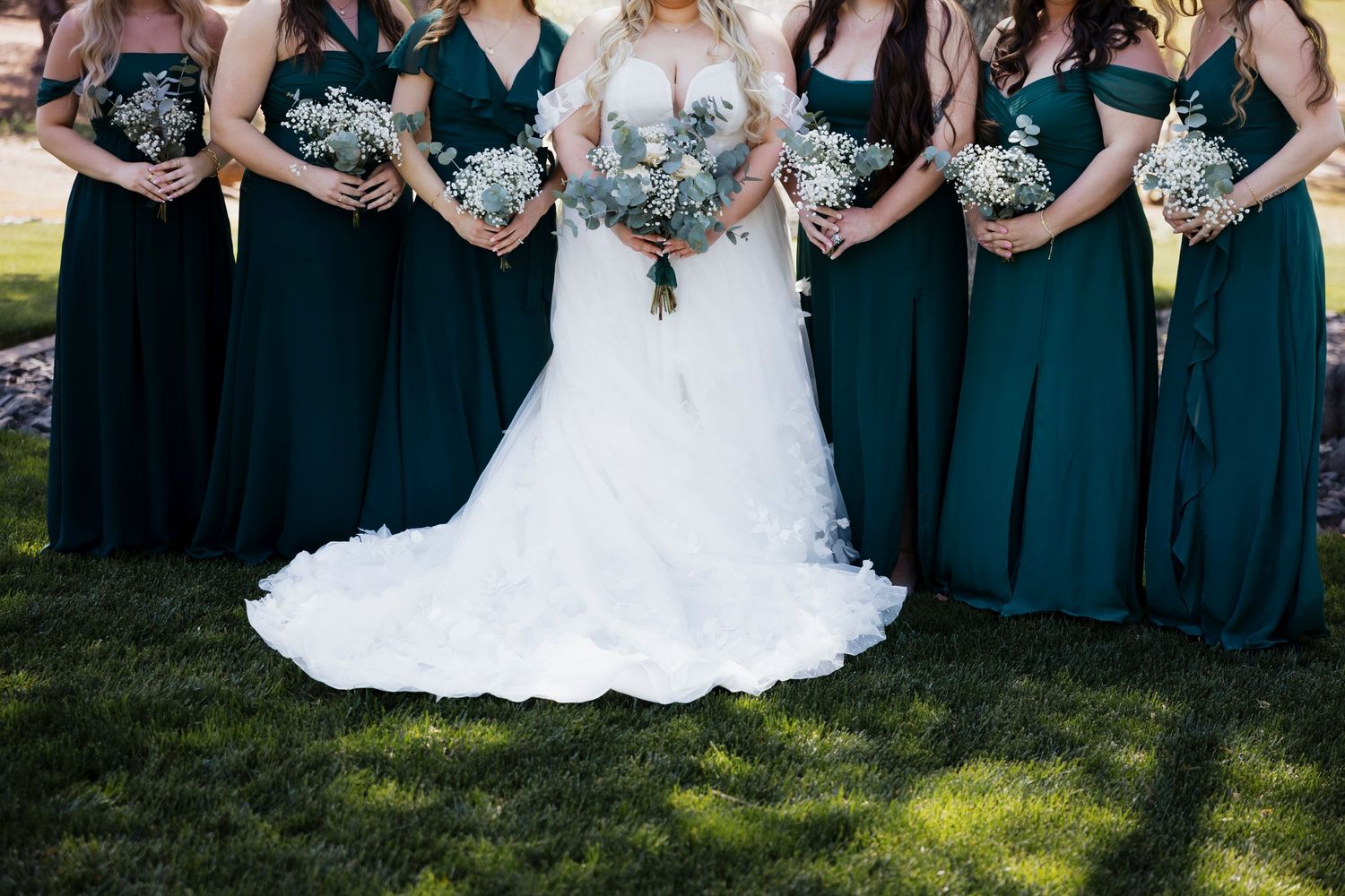 Bridesmaids in navy blue dresses stand together holding matching bouquets at an outdoor wedding ceremony.