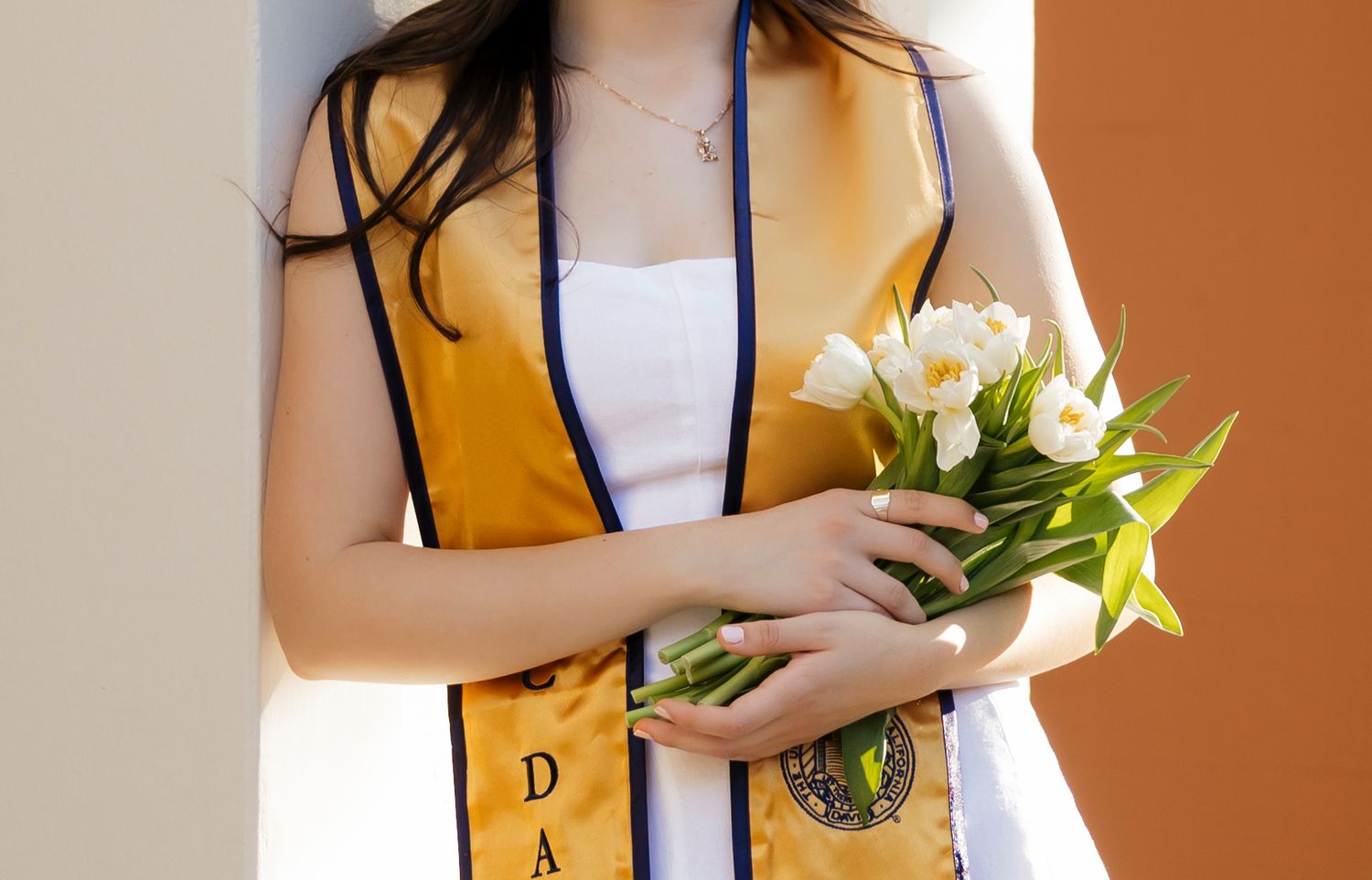 White tulips being held against an orange background in a casual portrait style.
