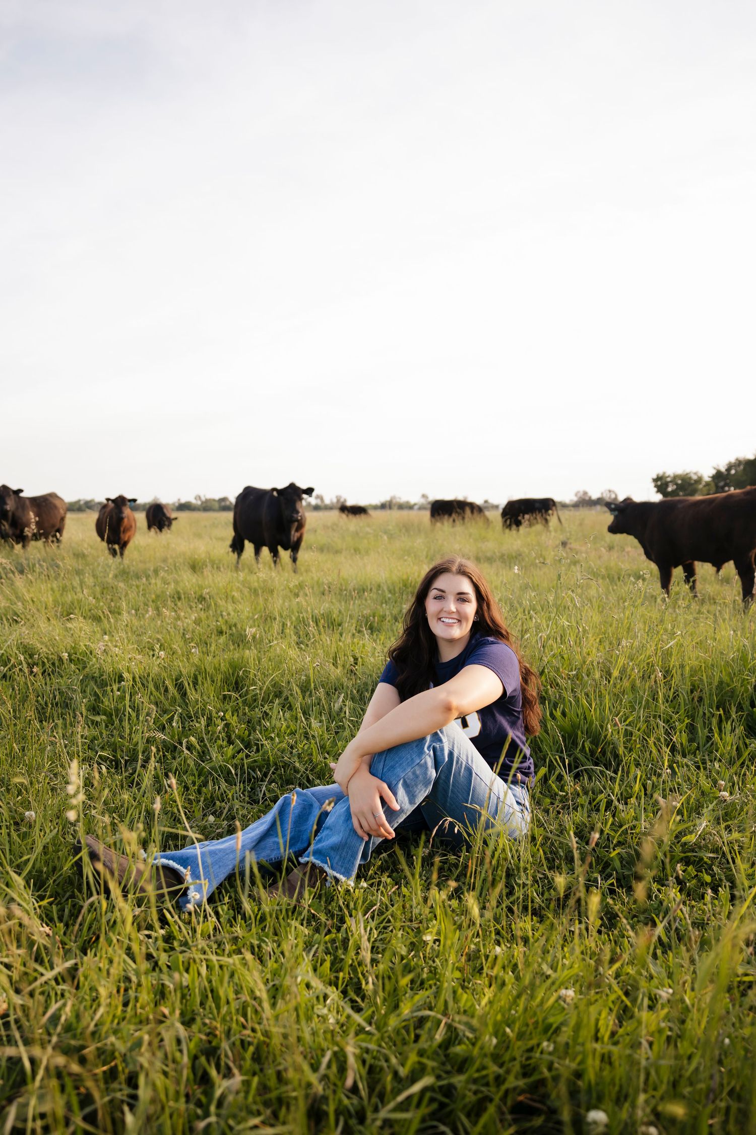 Senior relaxing in tall grass with cattle grazing in the background of a rural field.