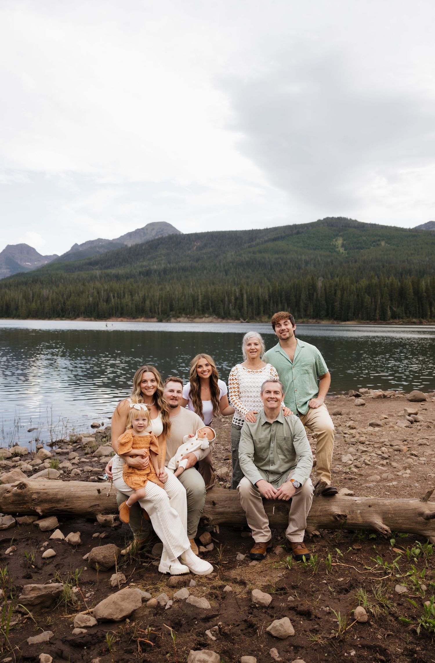 Extended family portrait session on rocky lakeshore with mountains in background.