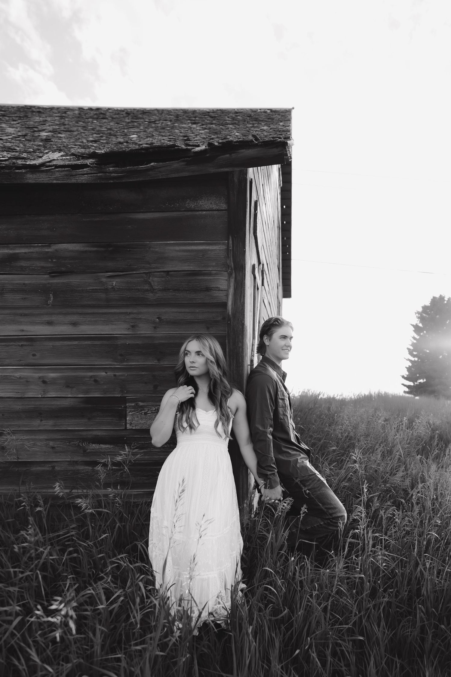 A couple poses against a rustic wooden barn wall in black and white photography.