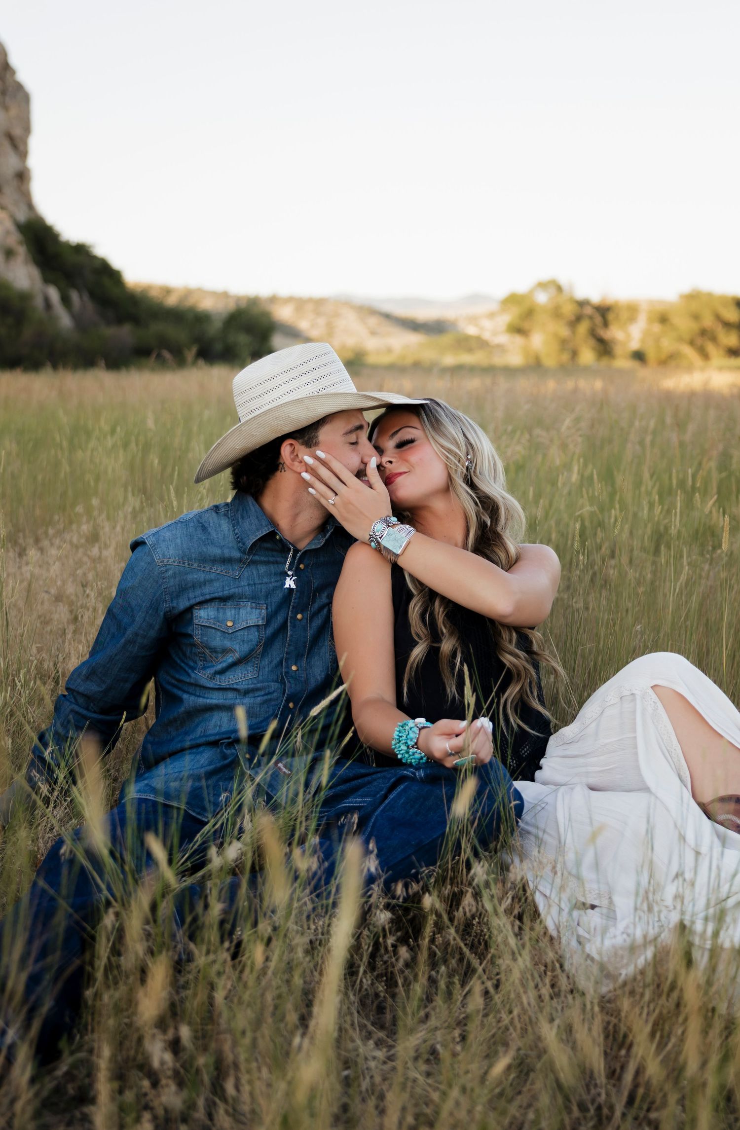 Couple shares intimate moment while sitting in tall grass during sunset.