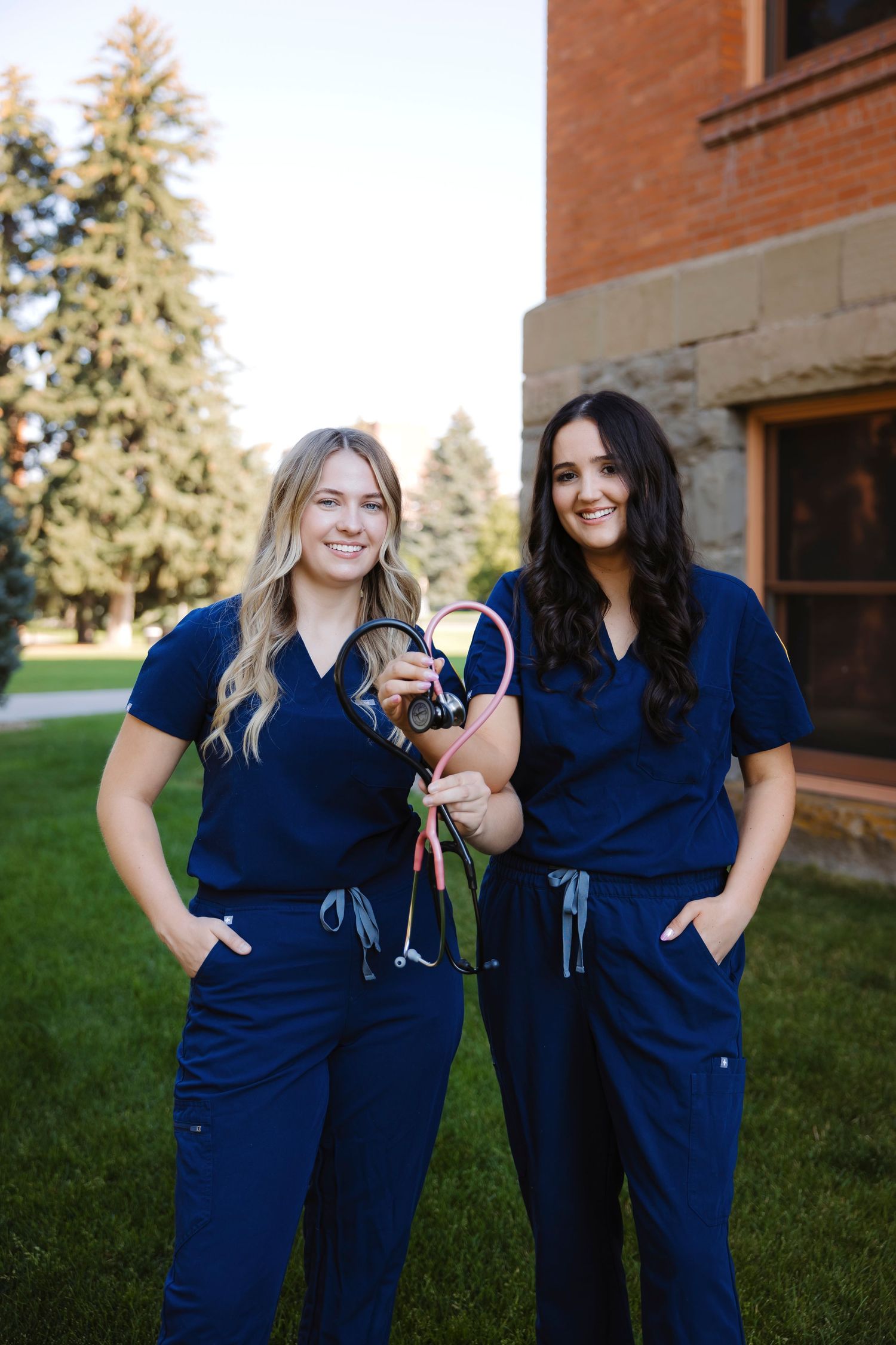 Two nursing students in blue scrubs pose together outdoors.