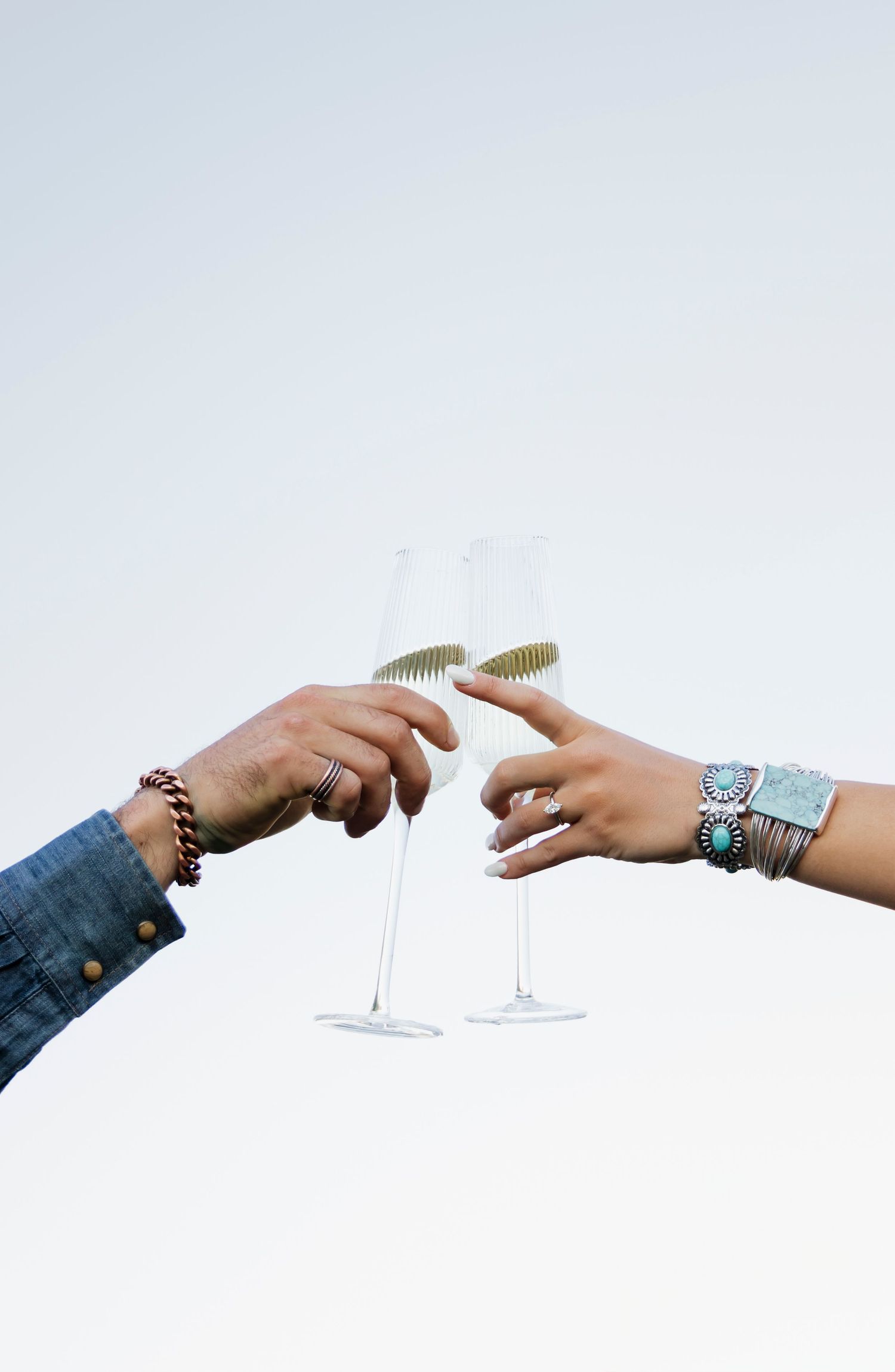 Two hands reach towards each other holding champagne glasses in a celebratory toast.
