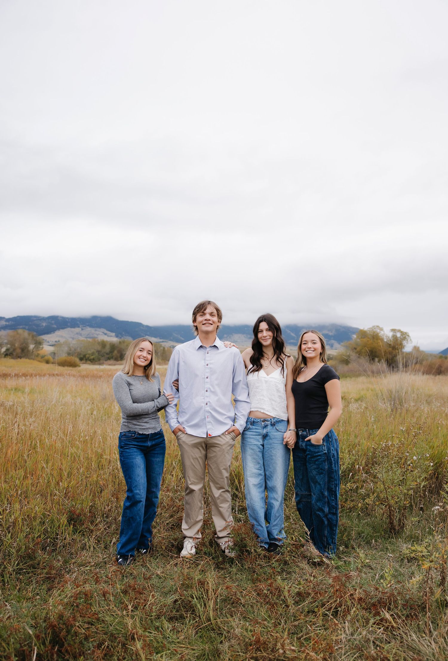 Group portrait in a grassy field with mountains in the background under cloudy skies.