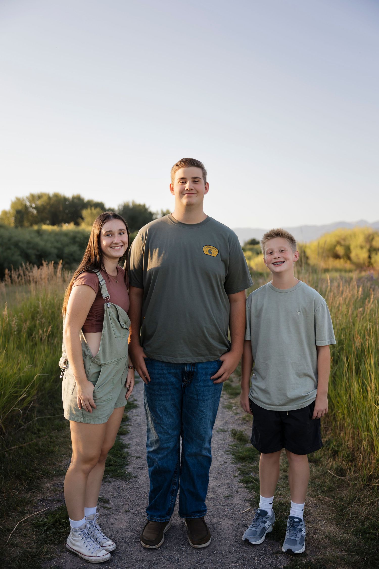 Casual family portrait on a dirt path surrounded by tall summer grass.