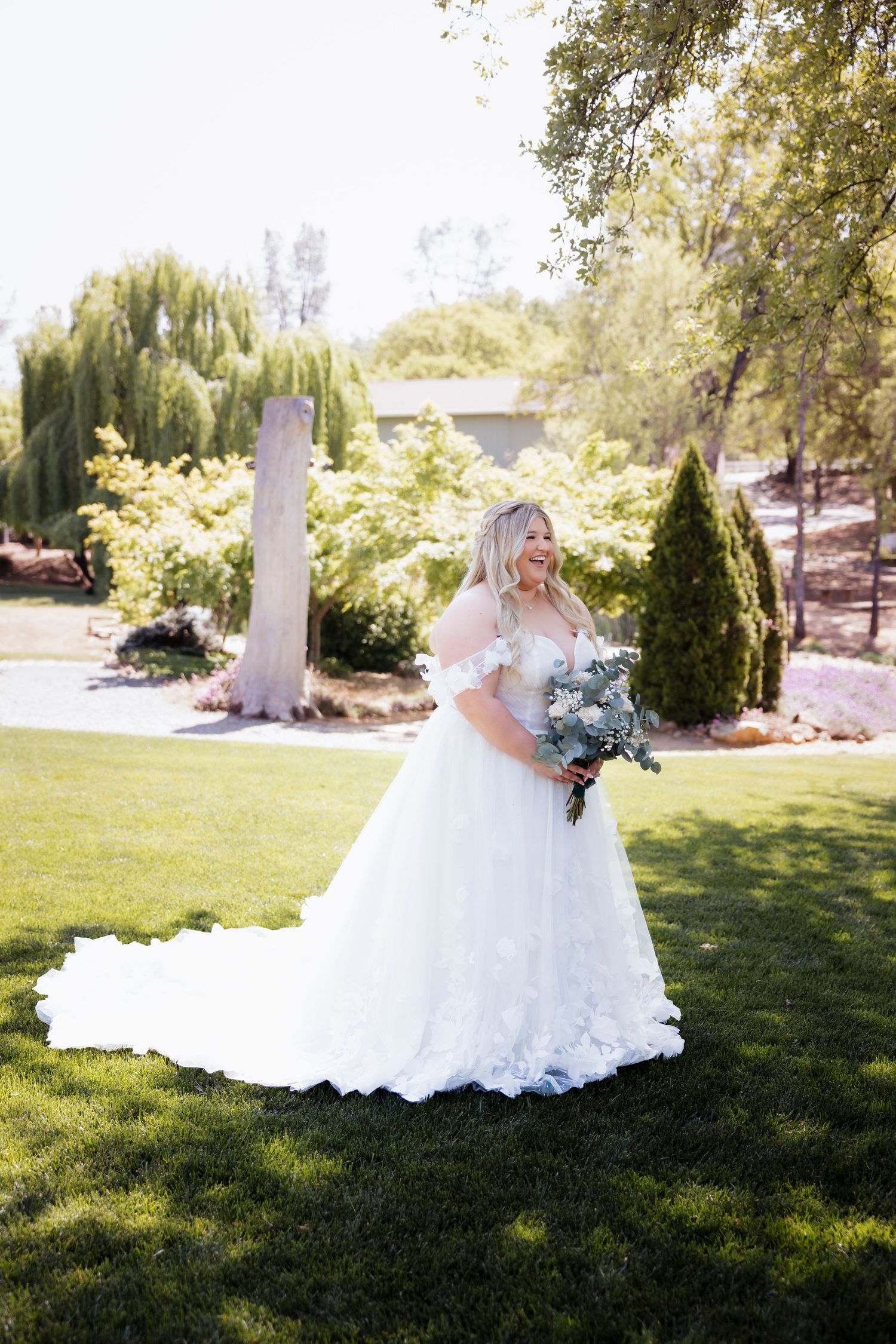 Bride in white lace gown posing on sunny green lawn.