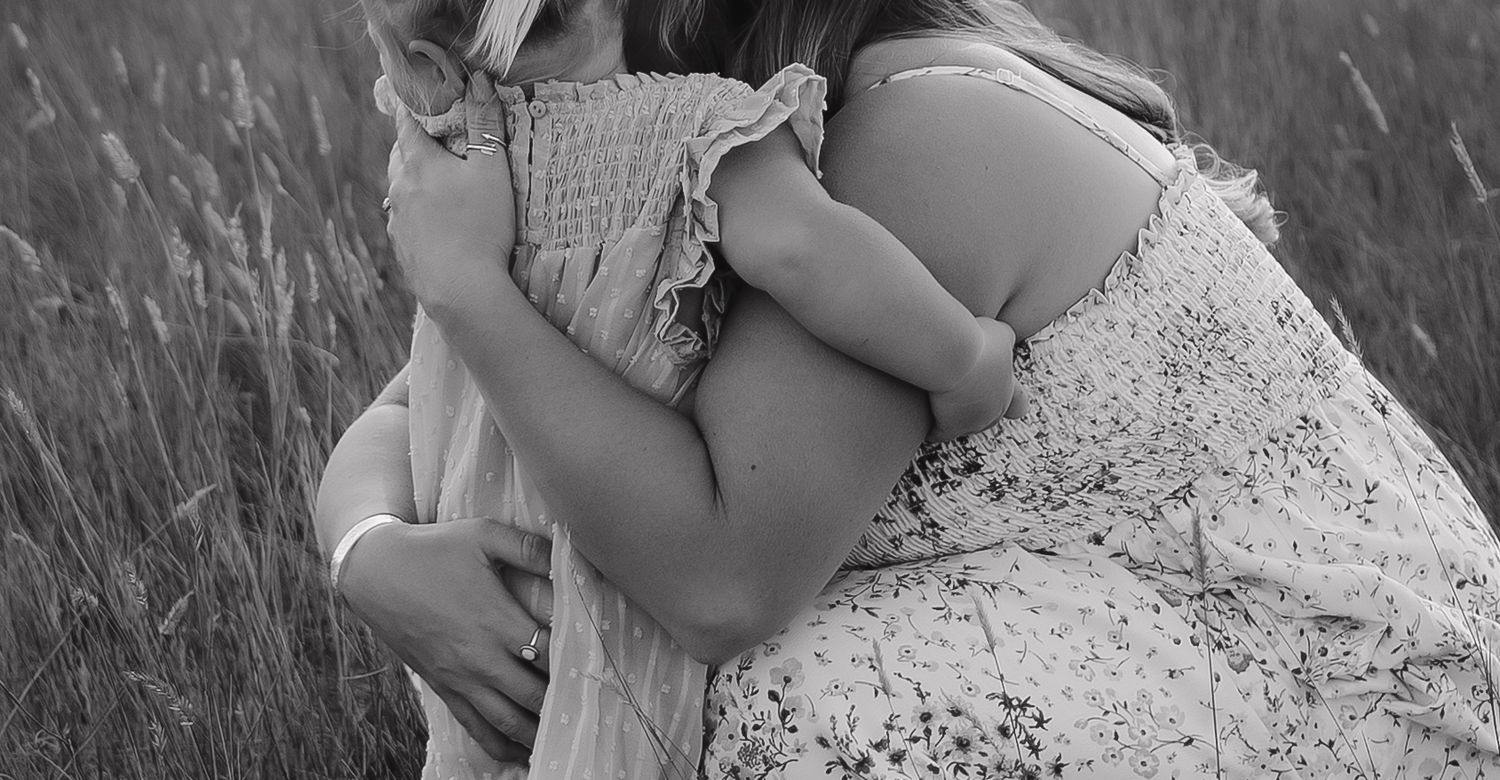 Intimate black and white family portrait in tall grass field.