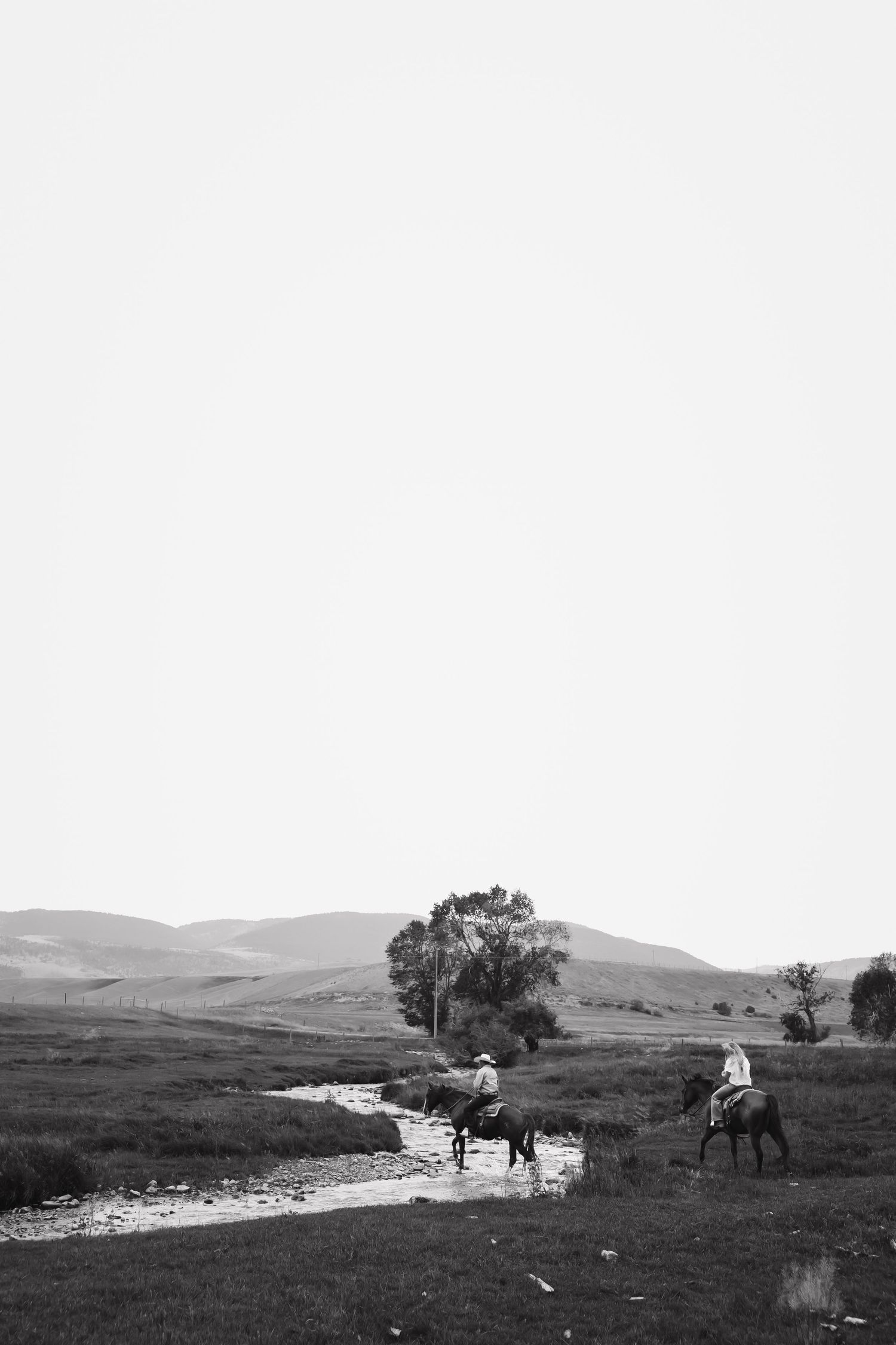 Horses and riders traverse a scenic mountain landscape with rolling hills and scattered trees.