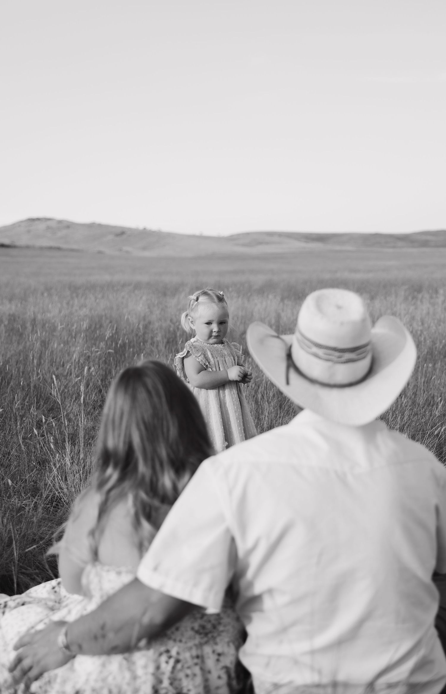 Black and white photograph of a family sharing an intimate moment in a grassy field.