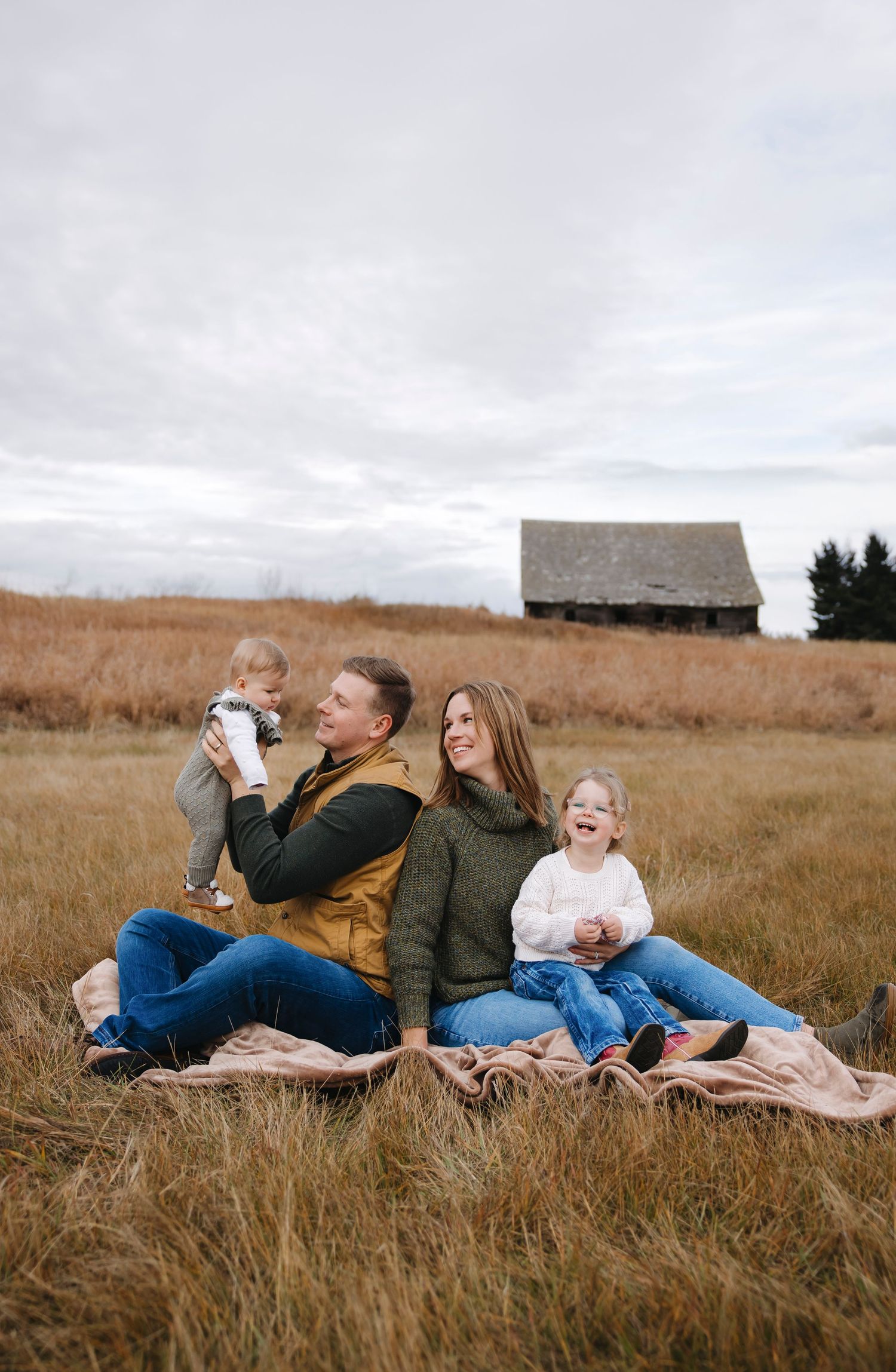 Family relaxing on blanket in autumn field with mountains in distance.
