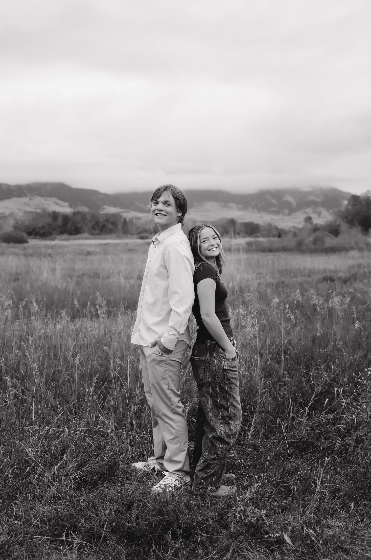 Black and white portrait of couple standing back-to-back in tall grass field.