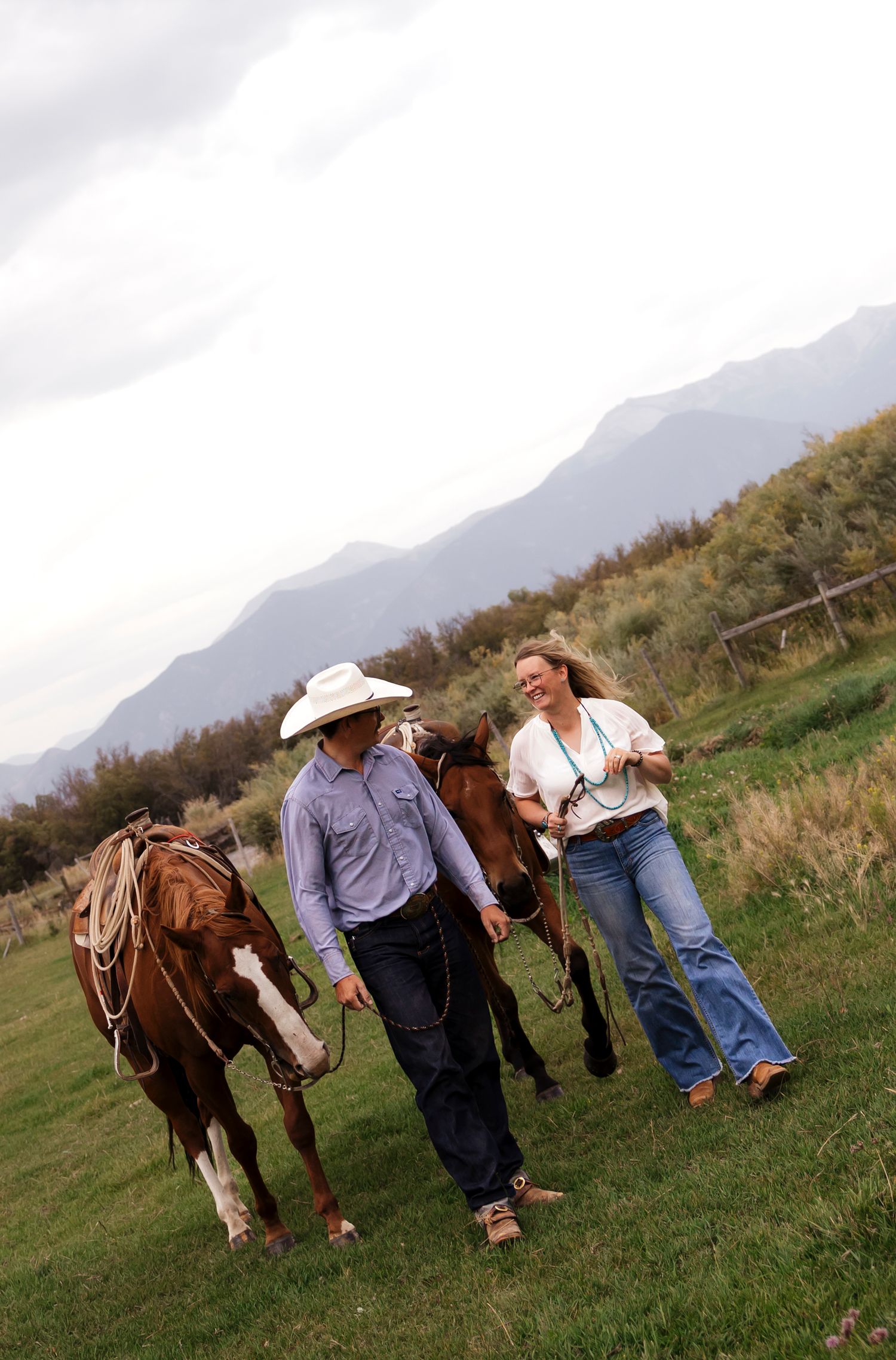 Couple walking alongside horses in a mountainous green landscape.