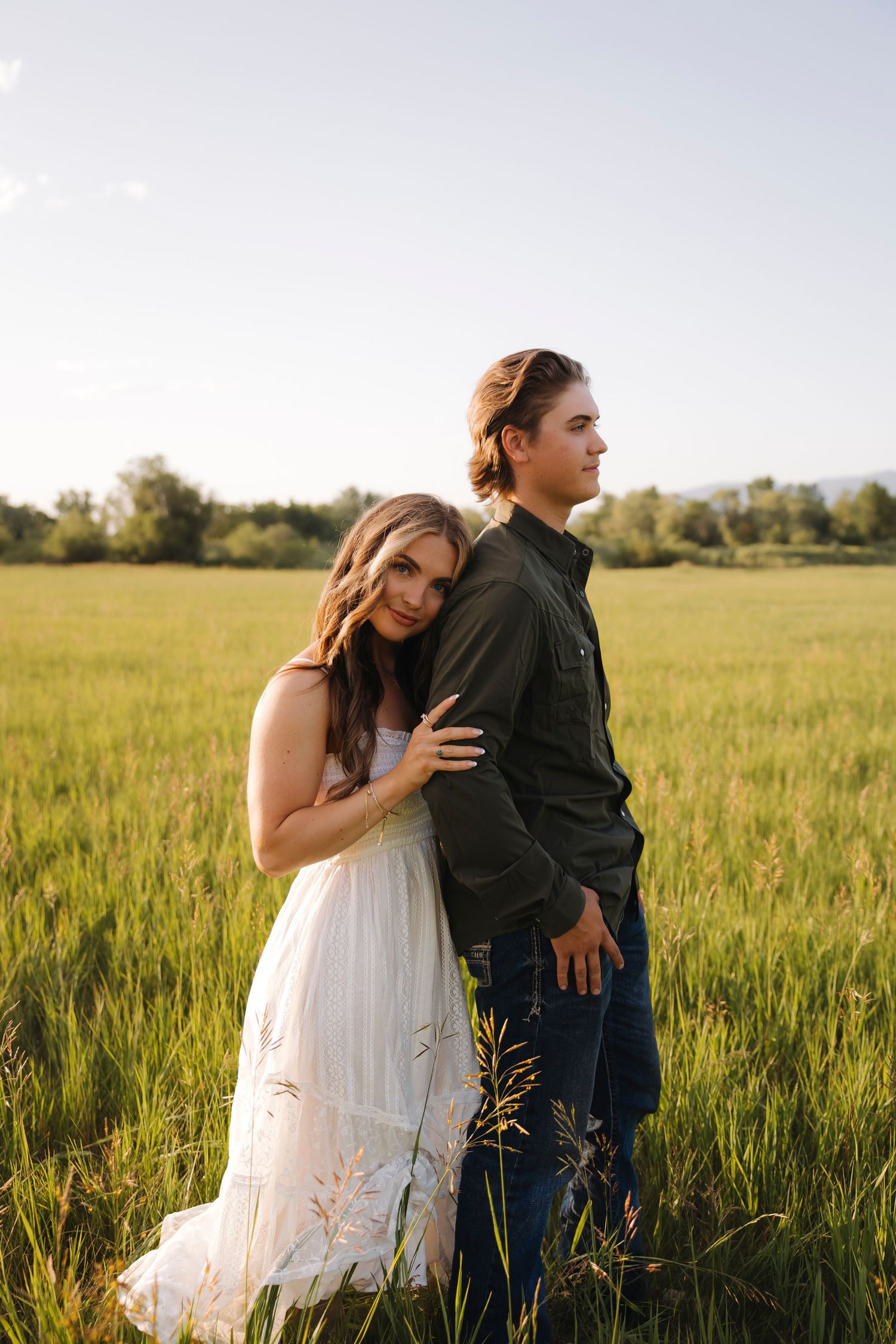 Couple embraces in a sunlit meadow with tall grass swaying around them.