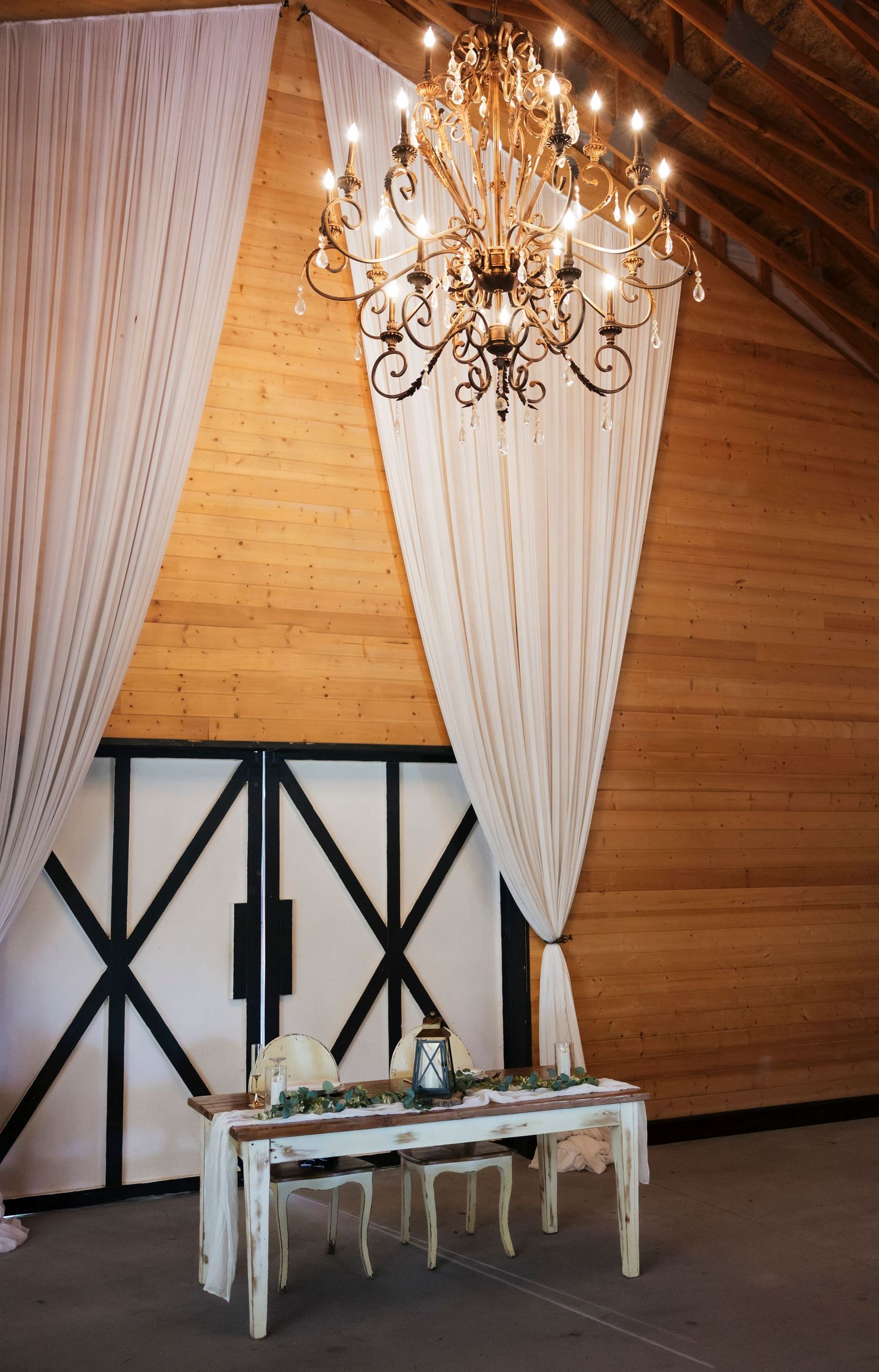 Modern barn venue interior with white draping, chandeliers and black architectural accents.