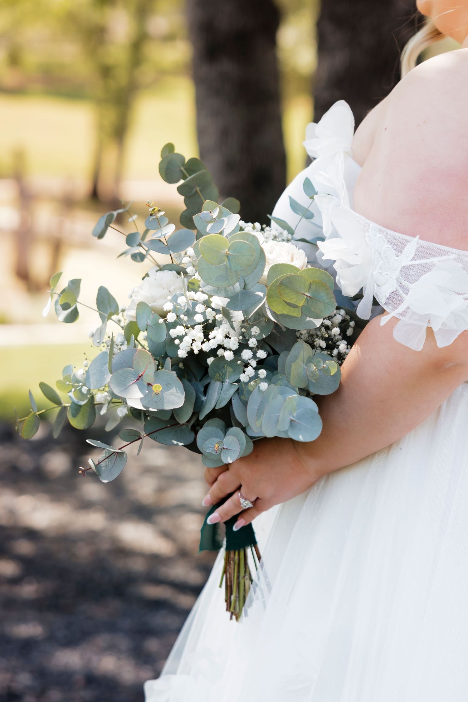 Fresh eucalyptus and baby's breath bouquet details against white wedding dress fabric.