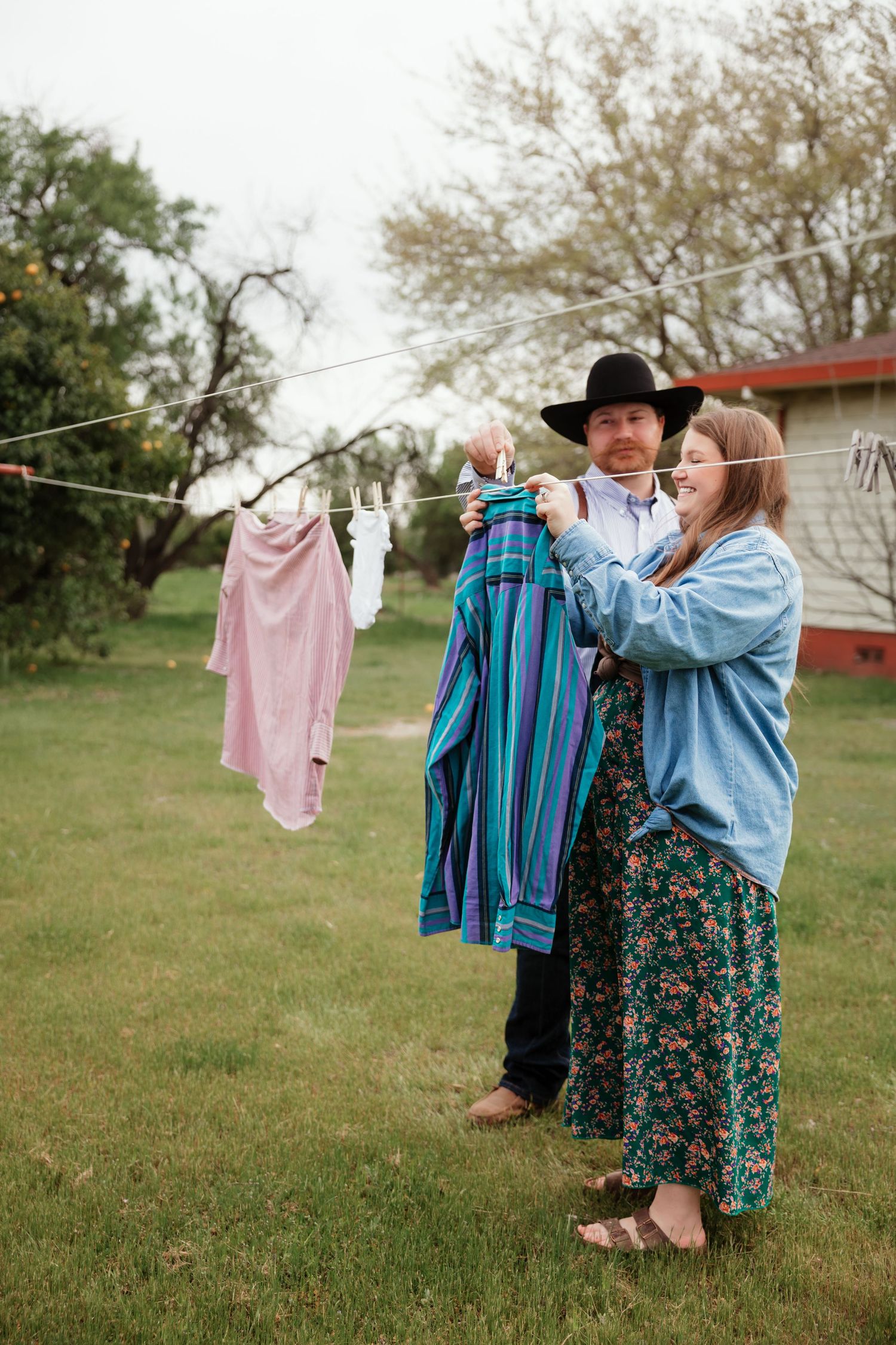 Colorful laundry hanging on clothesline in backyard with green grass and trees.