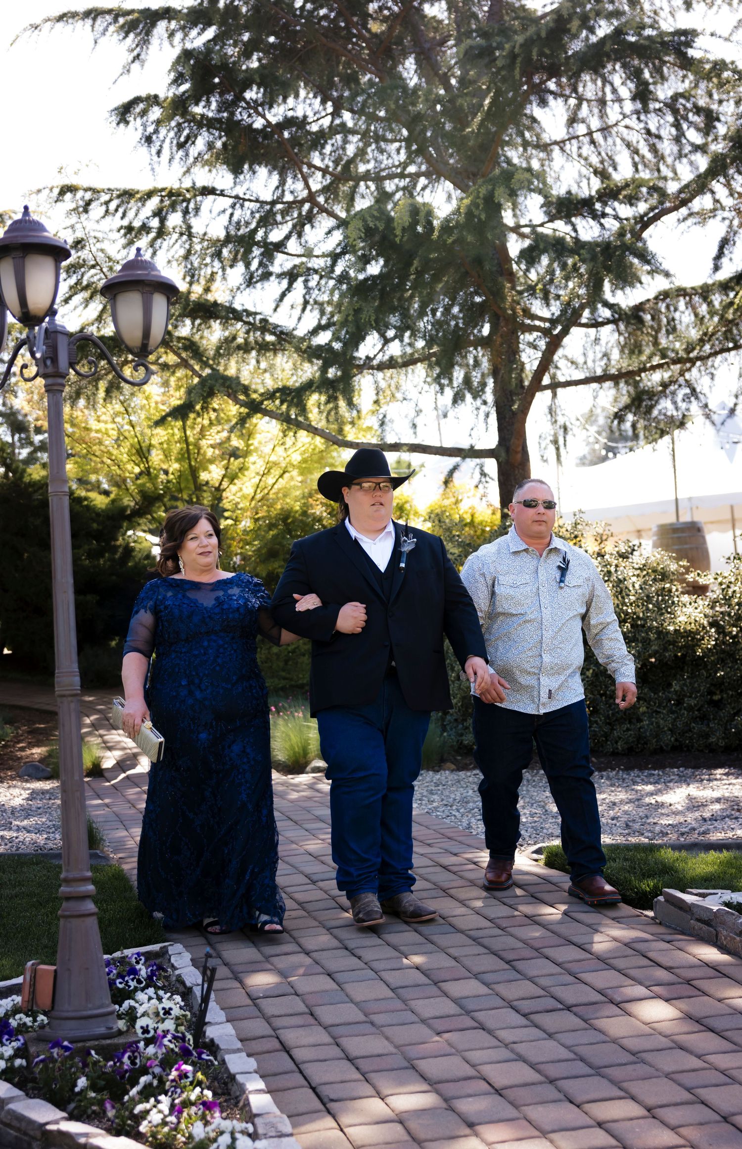 Groom and groom's parents walking down a brick pathway under decorative lamp posts.