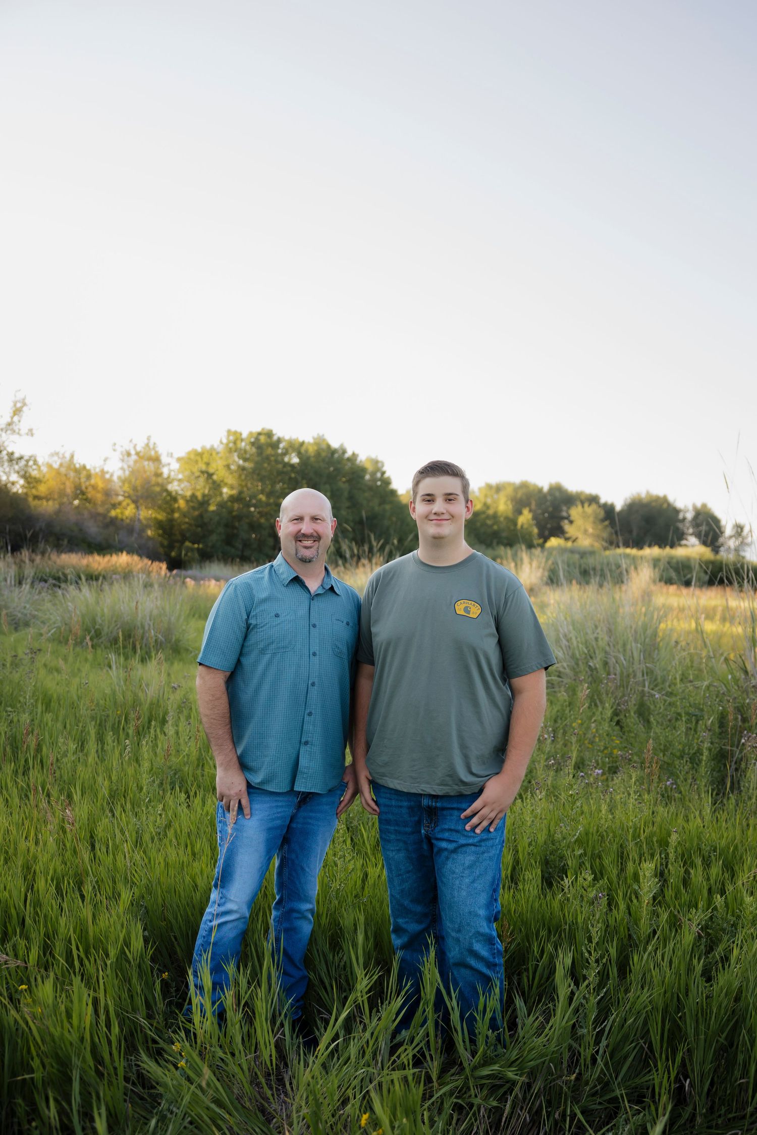 Family portrait of people standing together in a lush green field during golden hour.