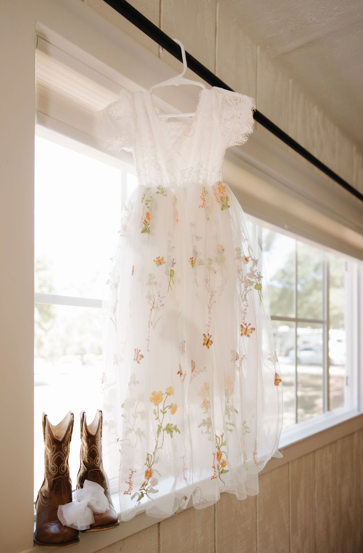 White lace curtains and brown cowboy boots displayed near a window.