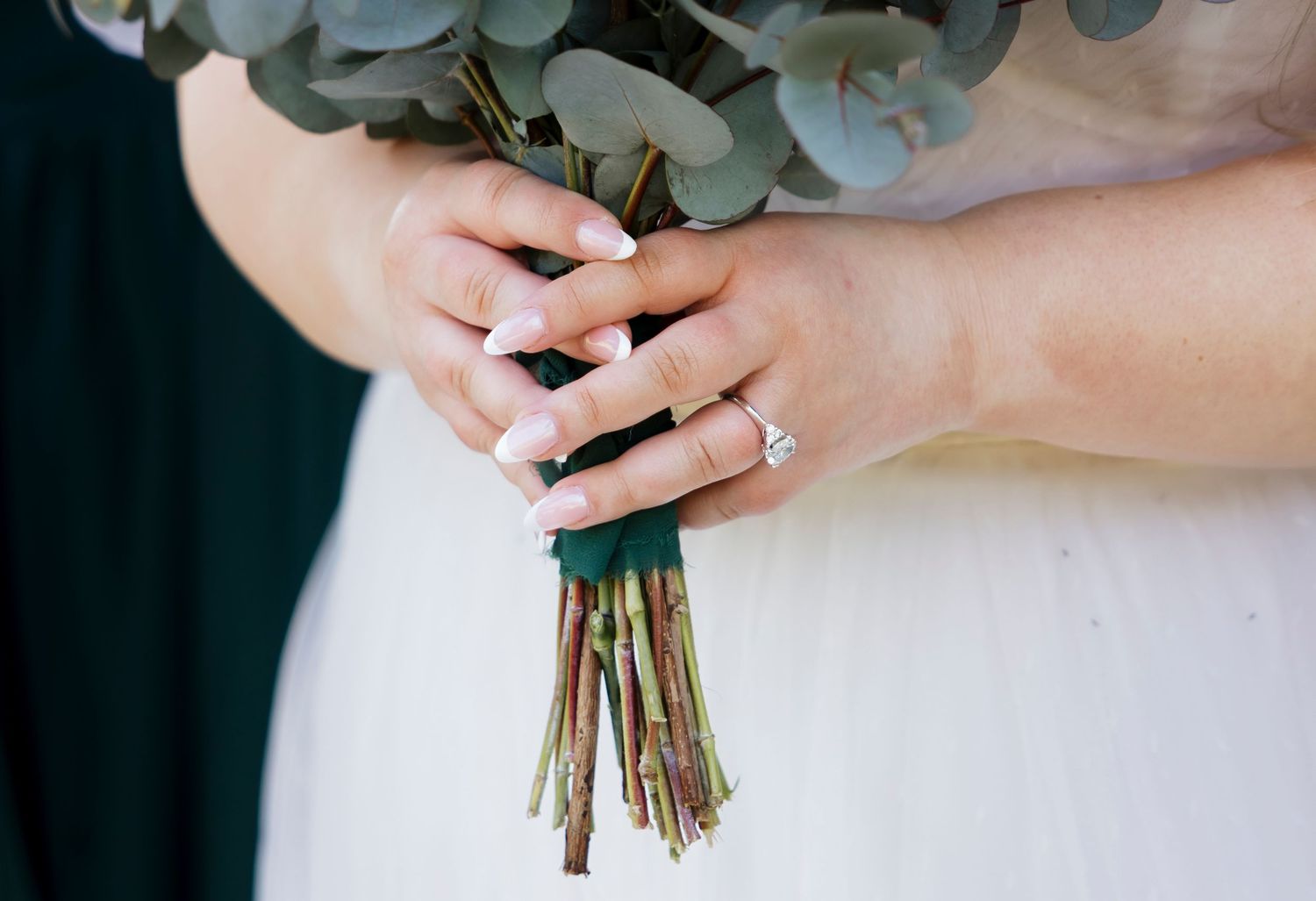 Elegant eucalyptus and white floral wedding bouquet held against a white dress.