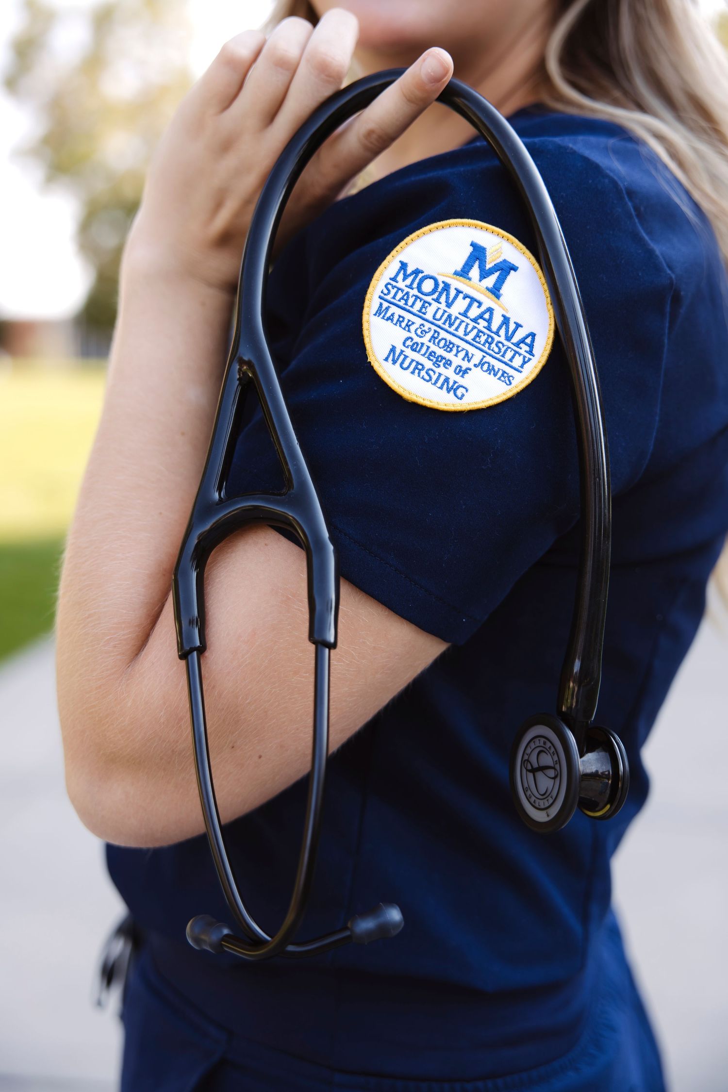 Close-up of medical stethoscope and Montana State University nursing patch on blue scrubs.
