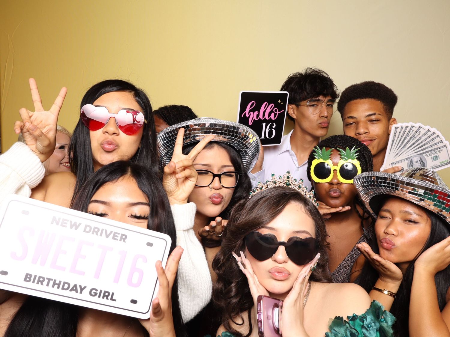 A group of friends pose together with fun props and sunglasses in a photo booth at a birthday celebration.