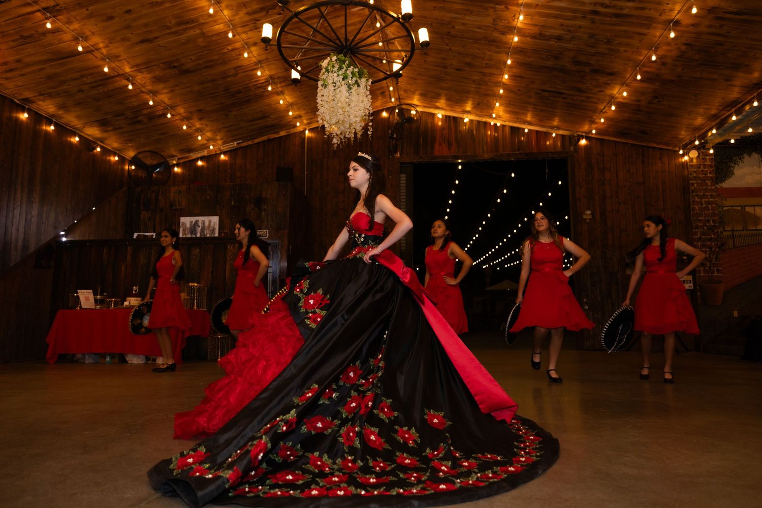 Elegant black and red ball gowns in a rustic venue with string lights and chandeliers.