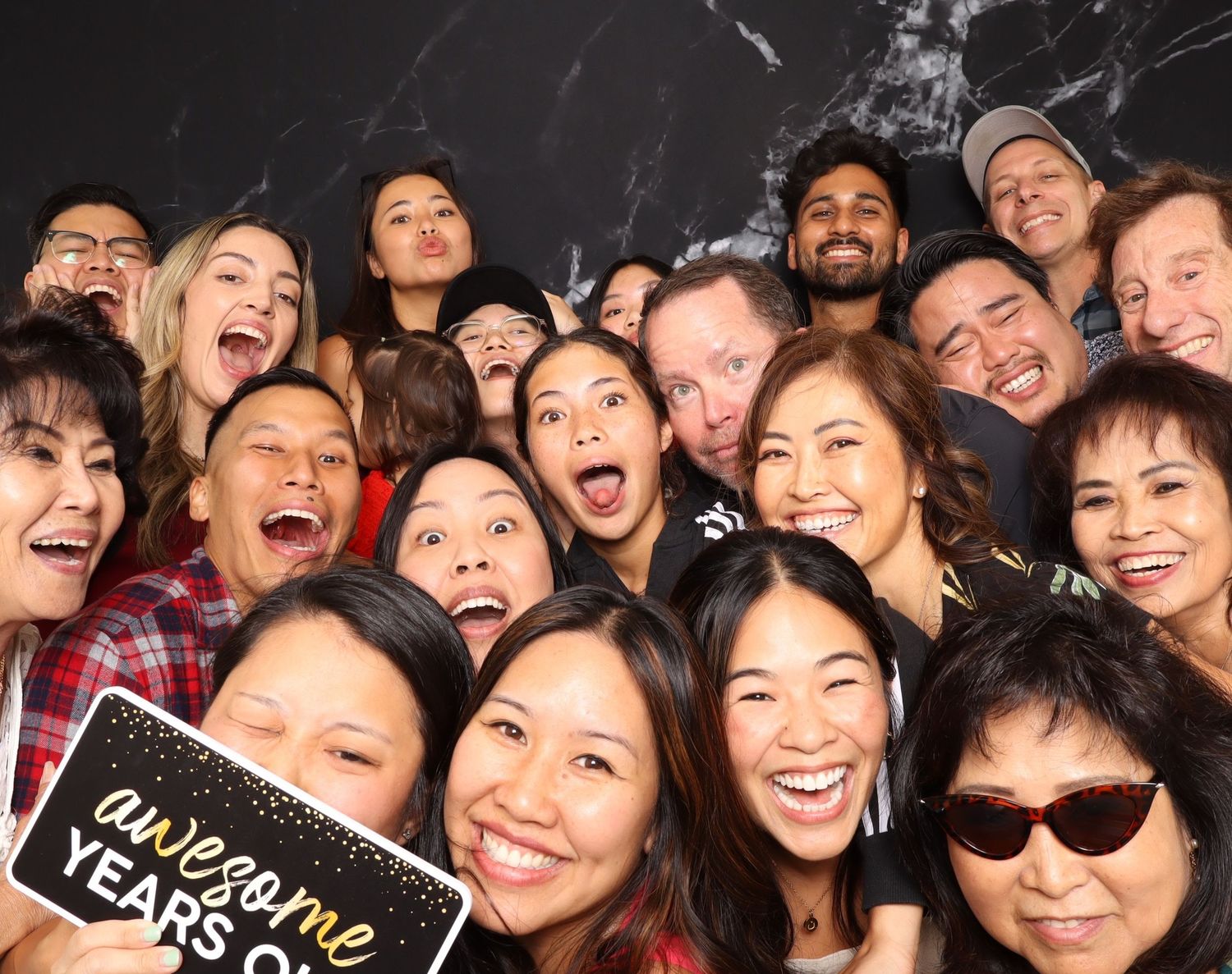A large group of diverse, smiling people posing together at a celebration, one holding an 