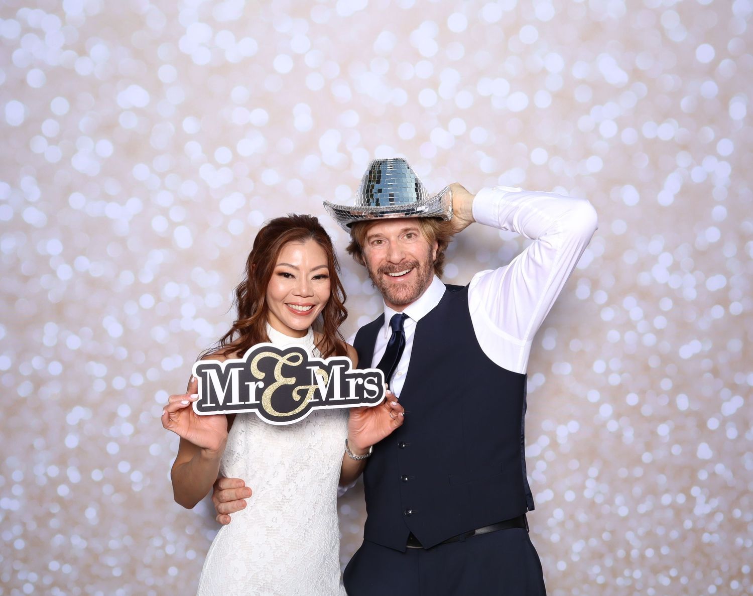 A couple poses together in formal wedding attire in front of a sparkly backdrop in a photo booth sequence.