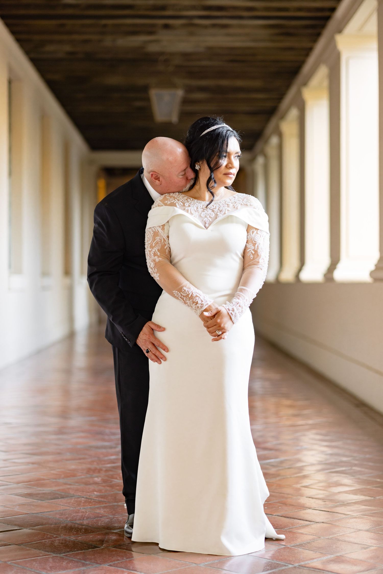 A couple shares an intimate moment in an elegant colonnade hallway.