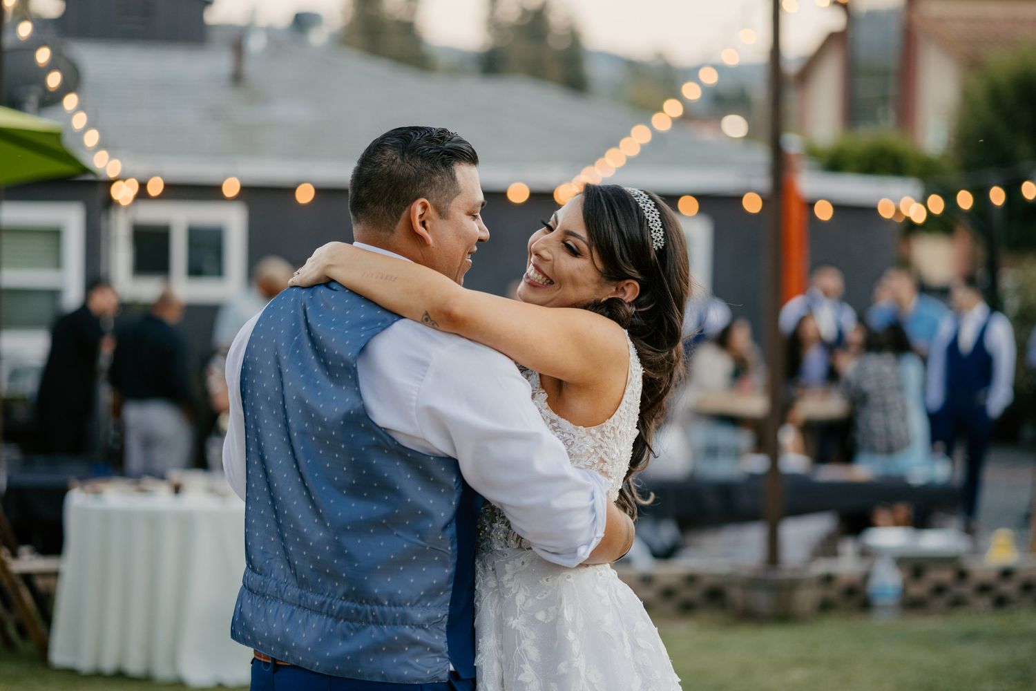 A couple shares a romantic dance moment at an outdoor wedding reception with string lights.